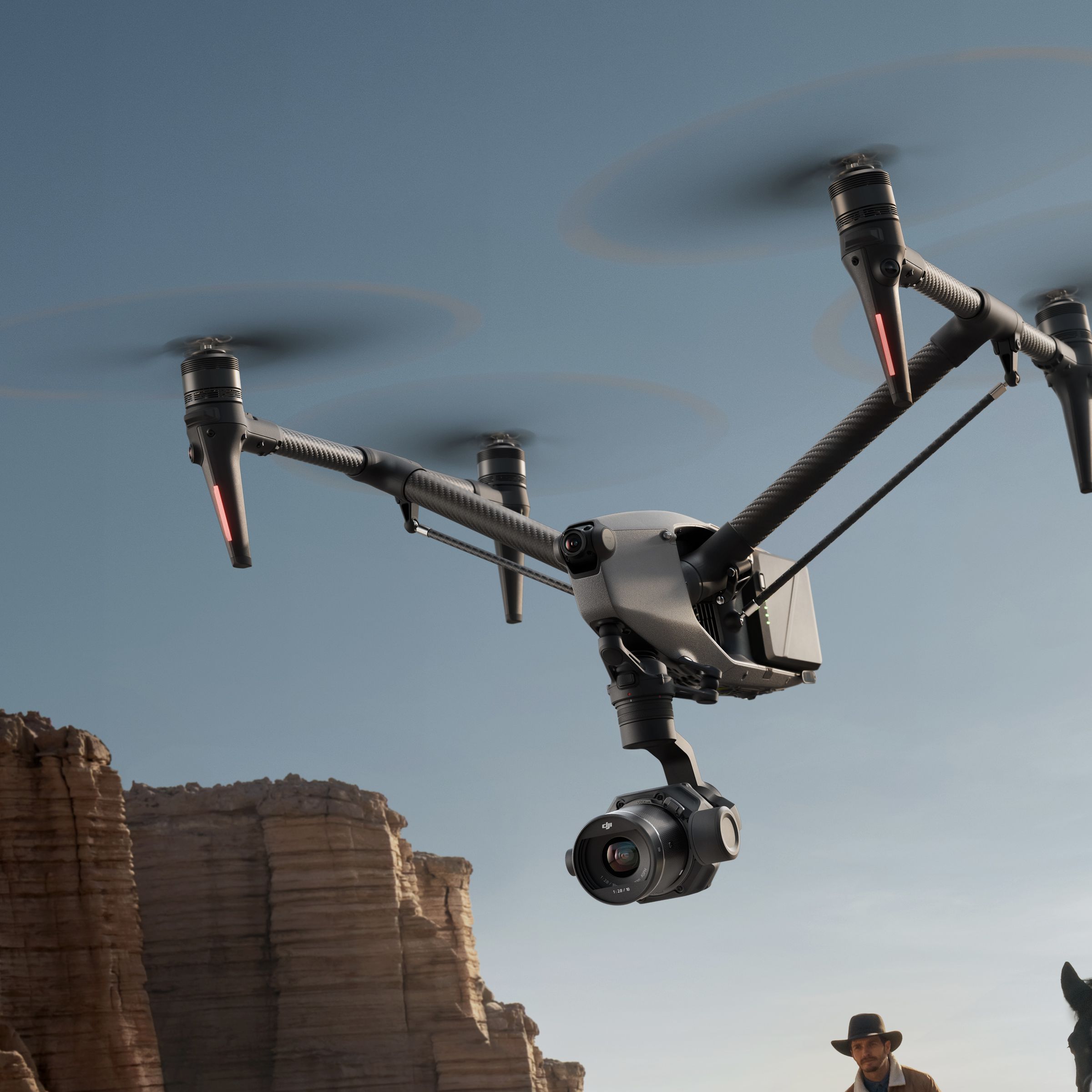 Inspire 3 drone flying low with cowboys on horses following it and cliffs in the background