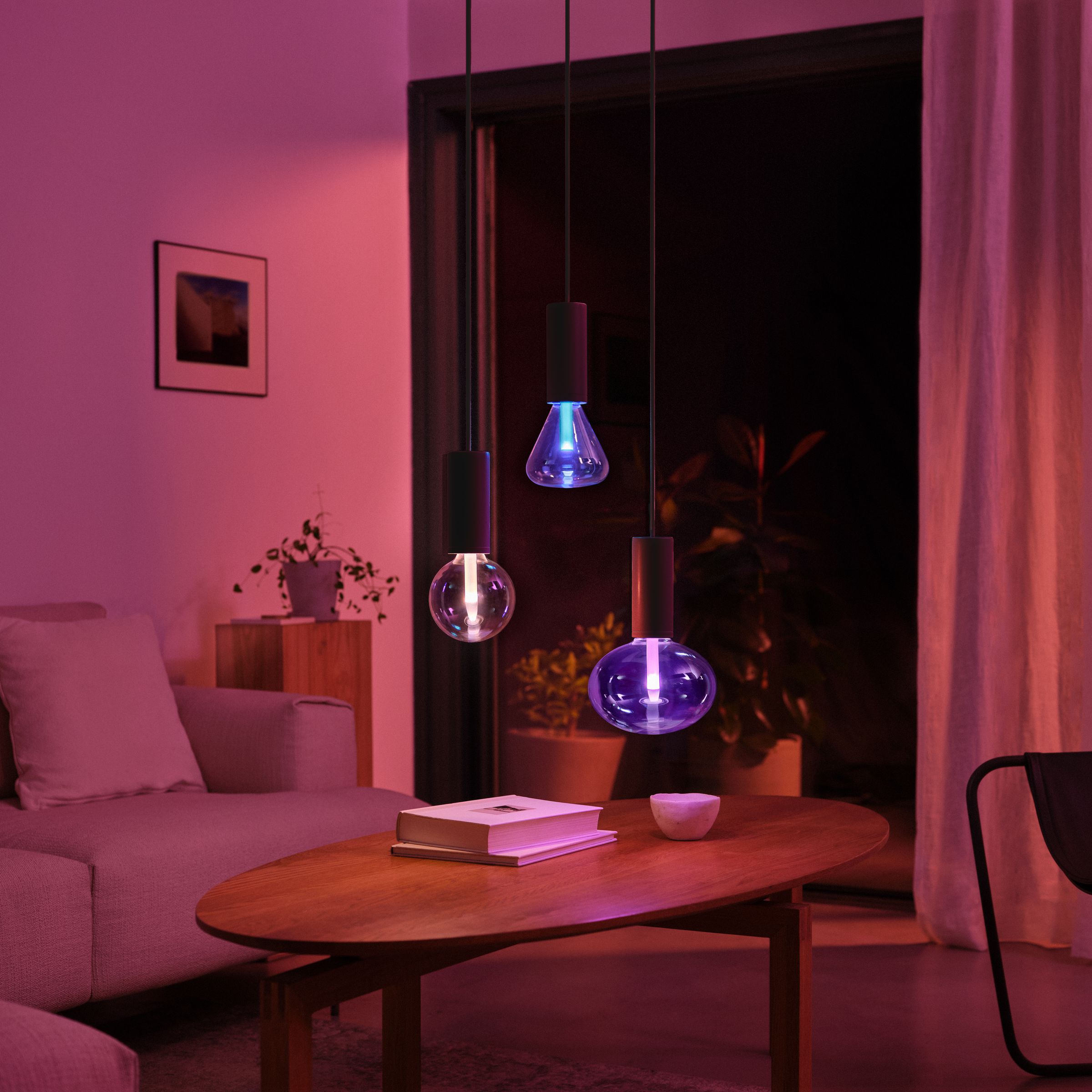 Three colorful lightbulbs hanging above a coffee table in a dark room.