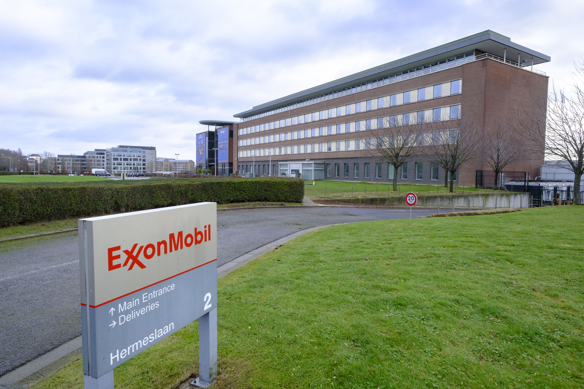 A sign with the ExxonMobil logo in the foreground with a large office building in the background.