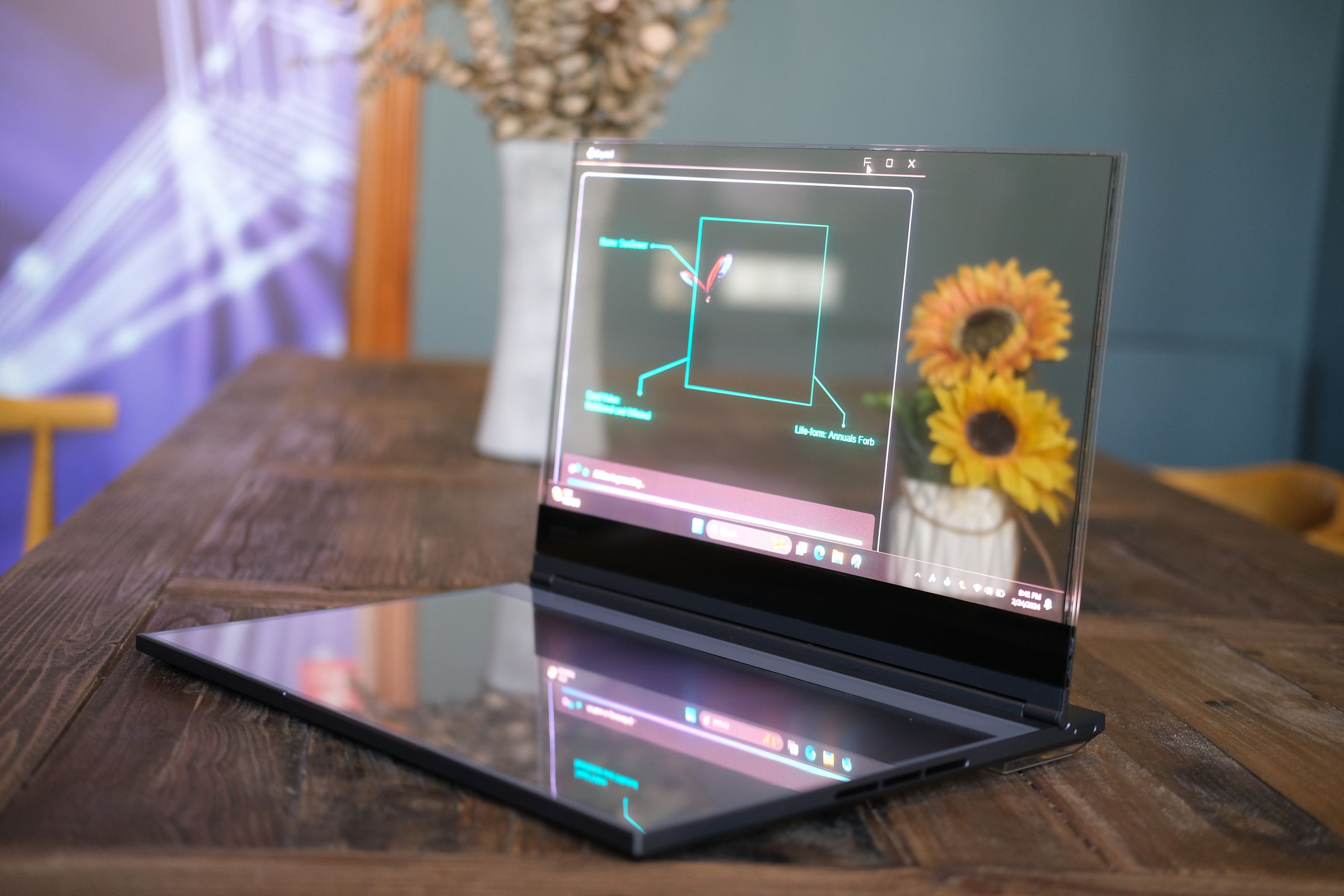 Transparent laptop with sunflowers visible behind it.
