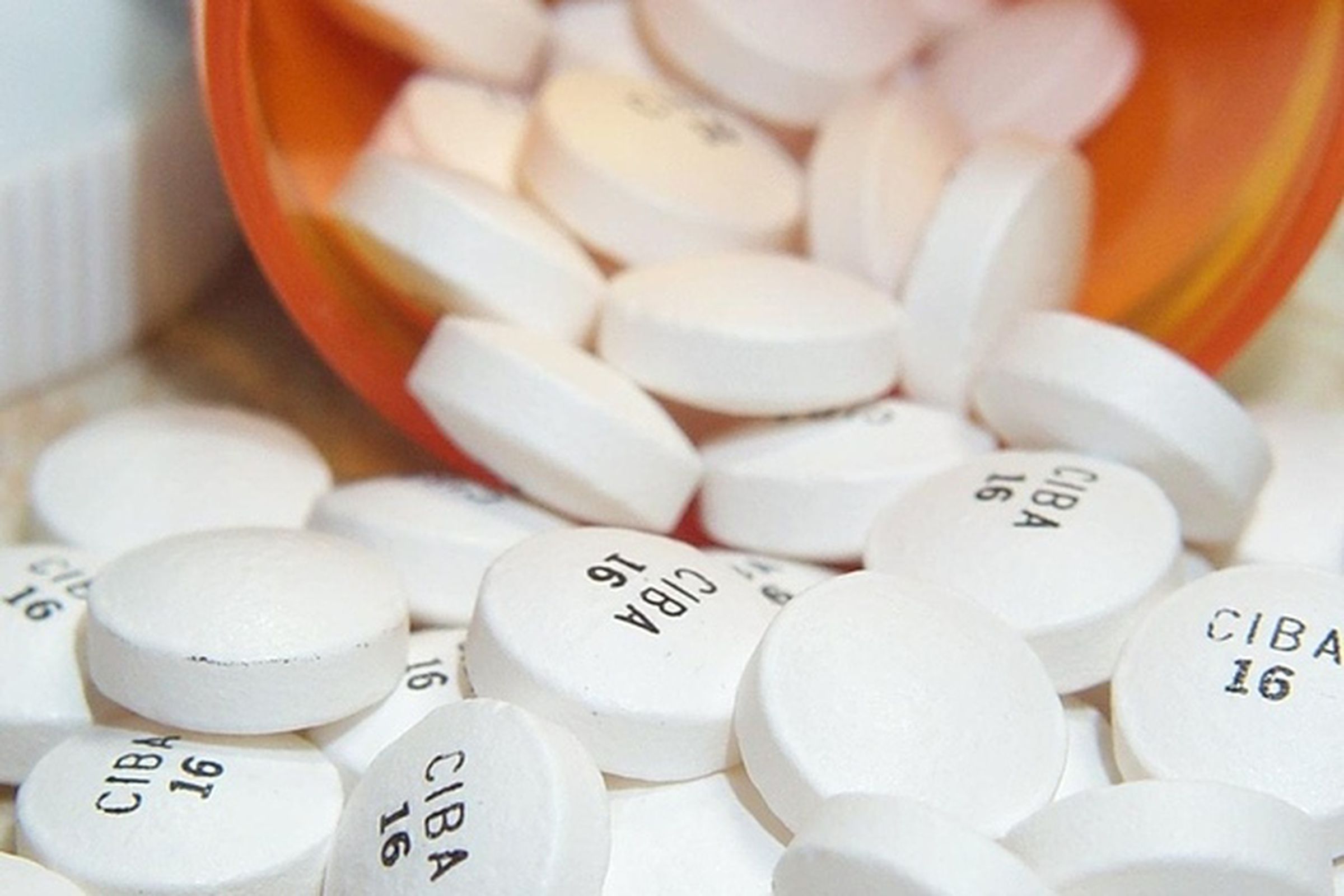 Round white pills spilling out of an orange pill bottle.
