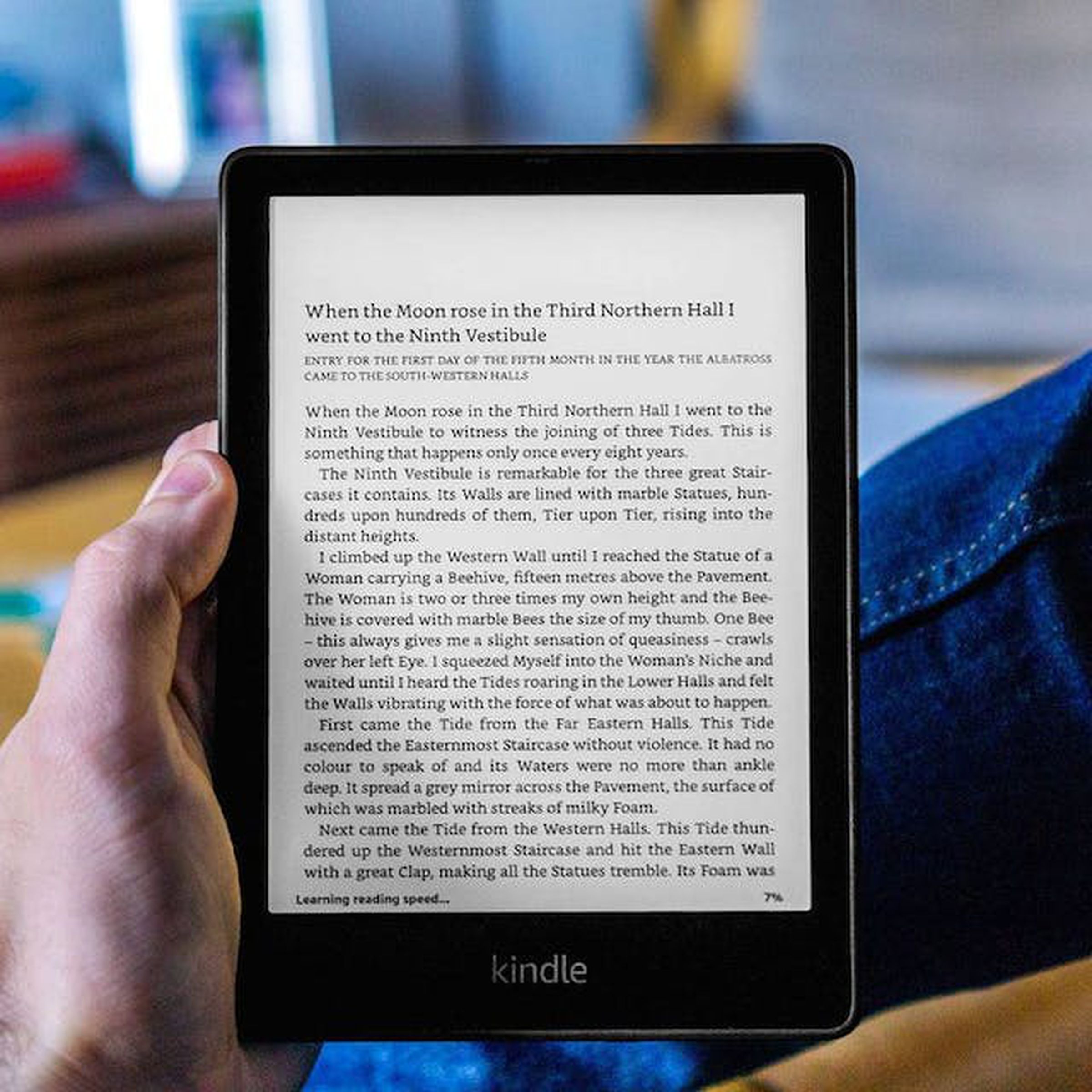 A hand holding the Kindle Paperwhite, which is on and displaying text from a book.