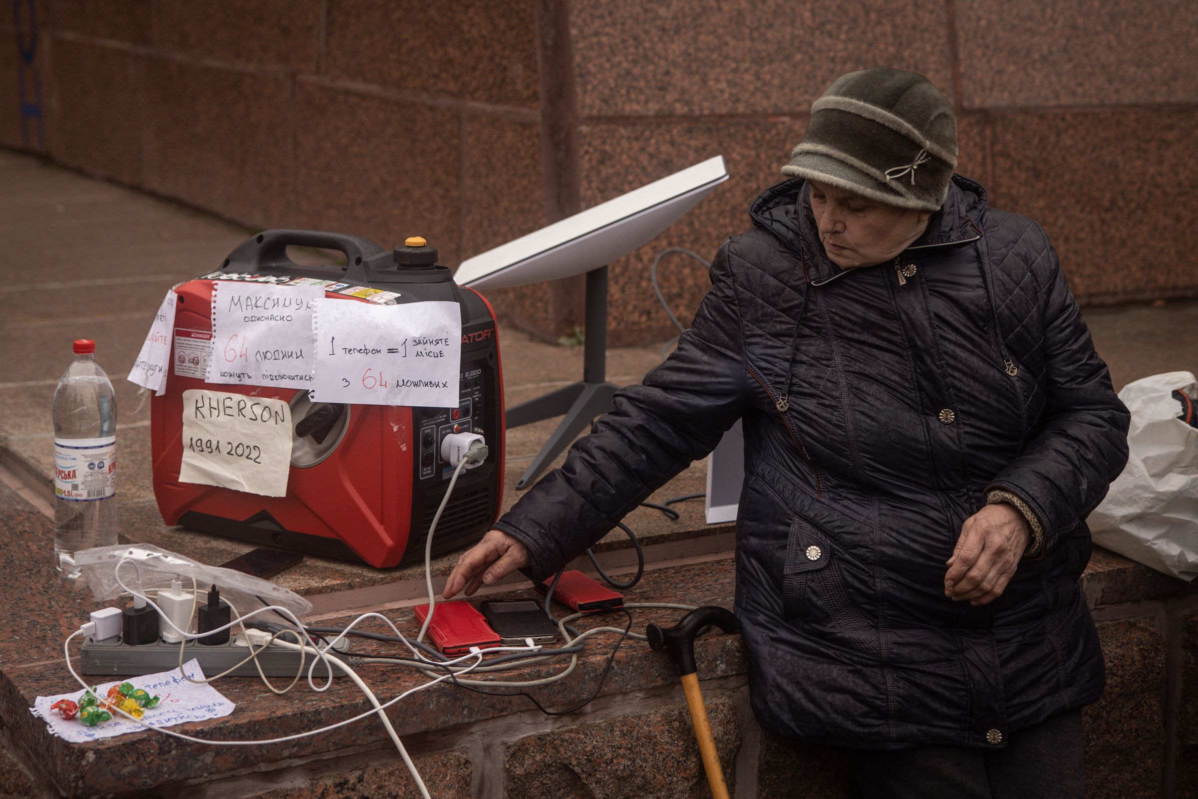 A resident waits for her phone to charge at a temporary charging point and internet hotspot via a Starlink device on November 17, 2022 in Kherson, Ukraine