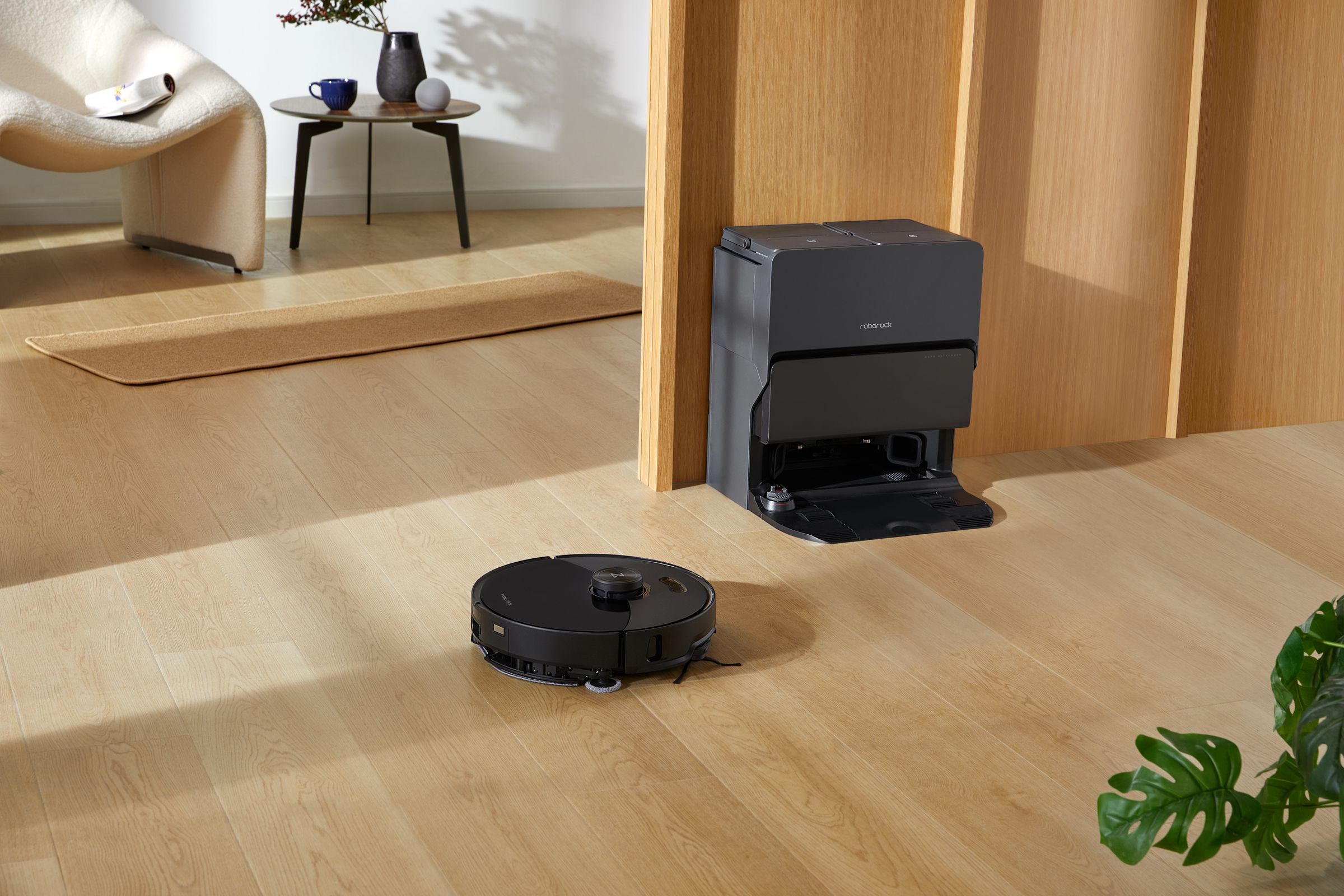 A black robot on a wood floor heading to a black charging base by a door.