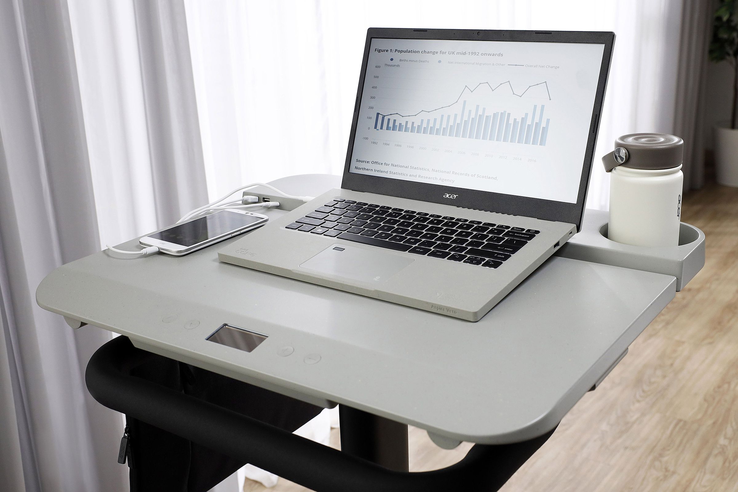 The desktop of the Acer eKinekt BD 3 bicycle desk, with a laptop, telephone, mug and a portable power bank on it.