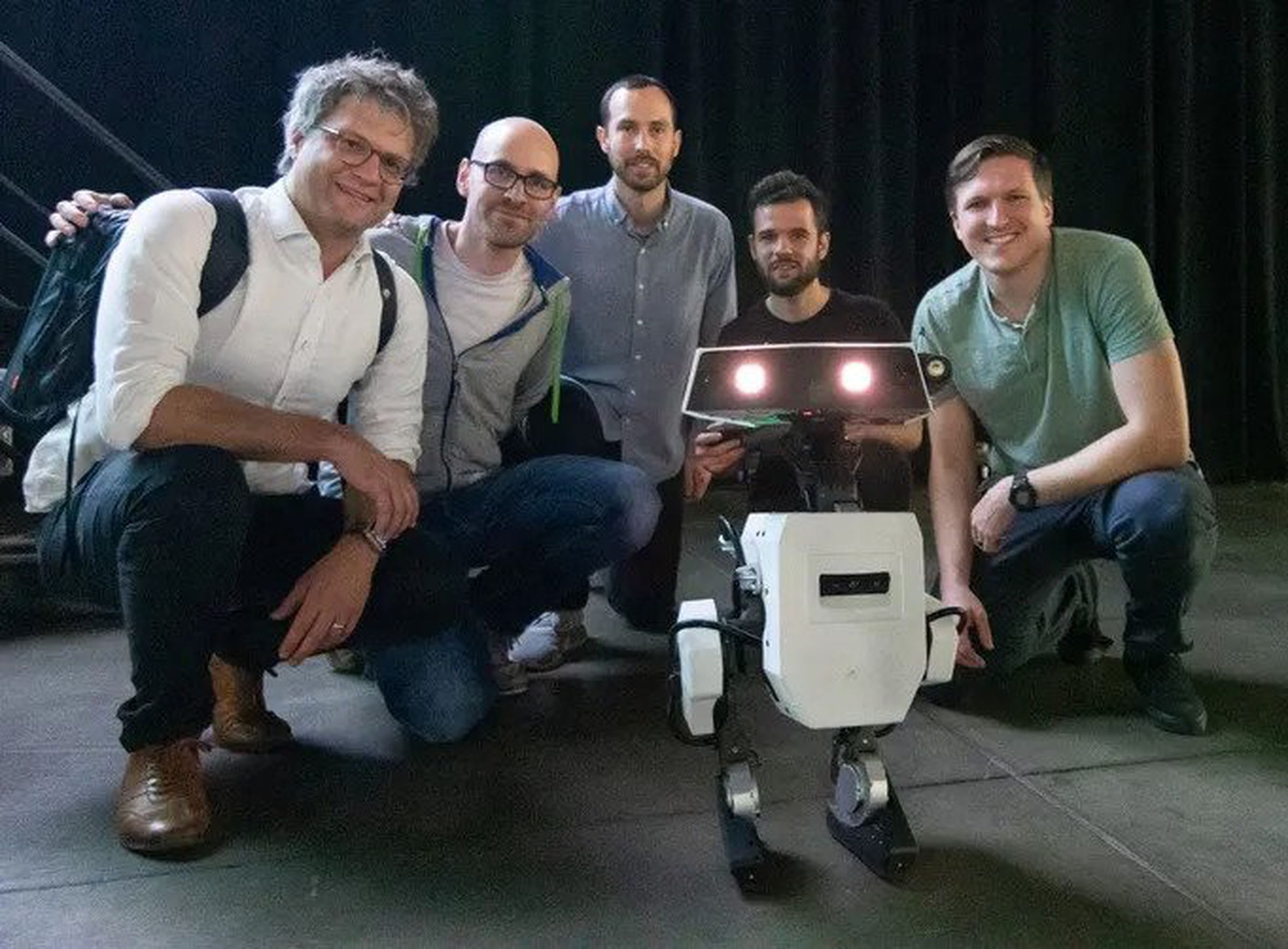 A group of Disney researchers gathered around a bipedal concept robot.