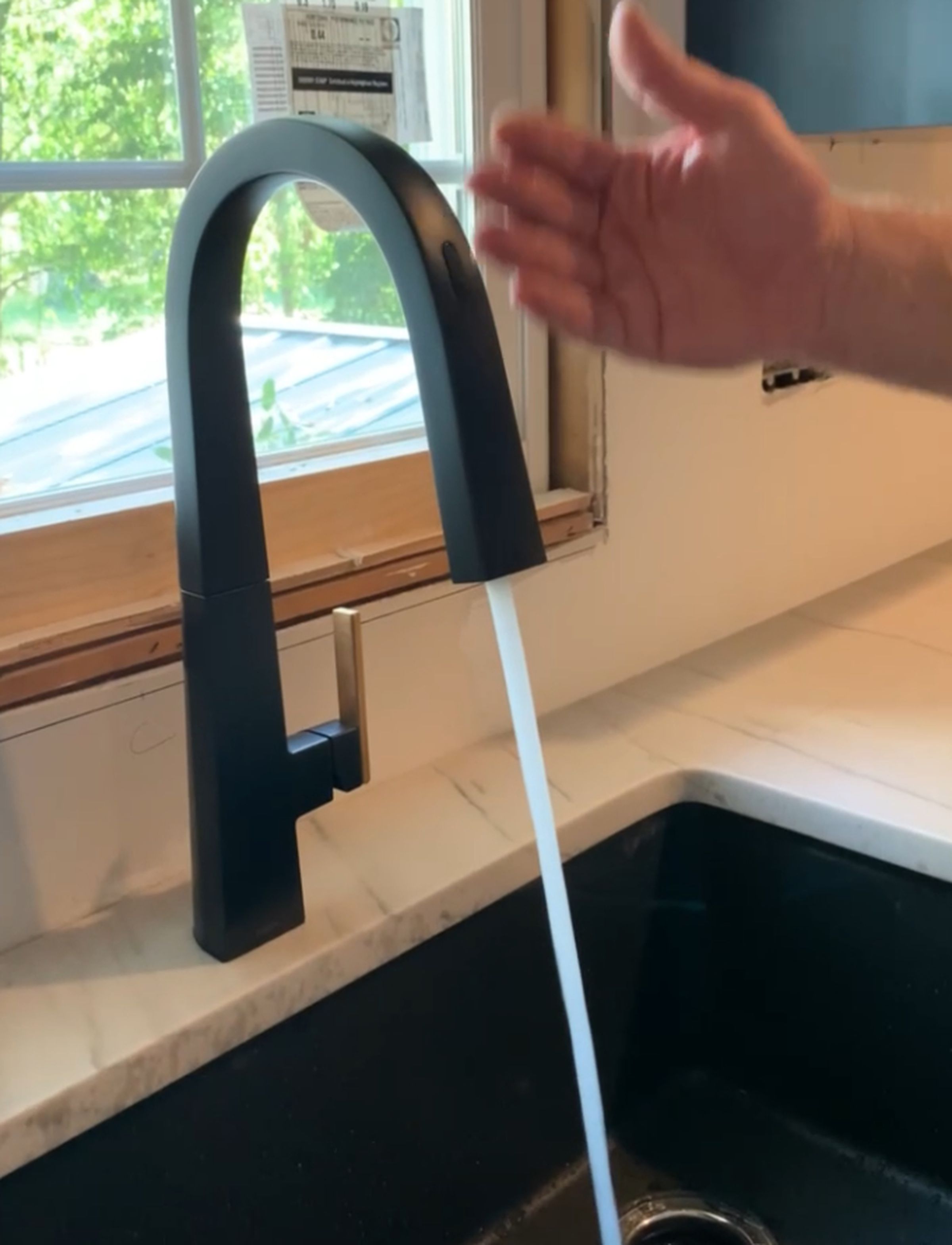 A dark gray faucet spouting water with a hand nearby.