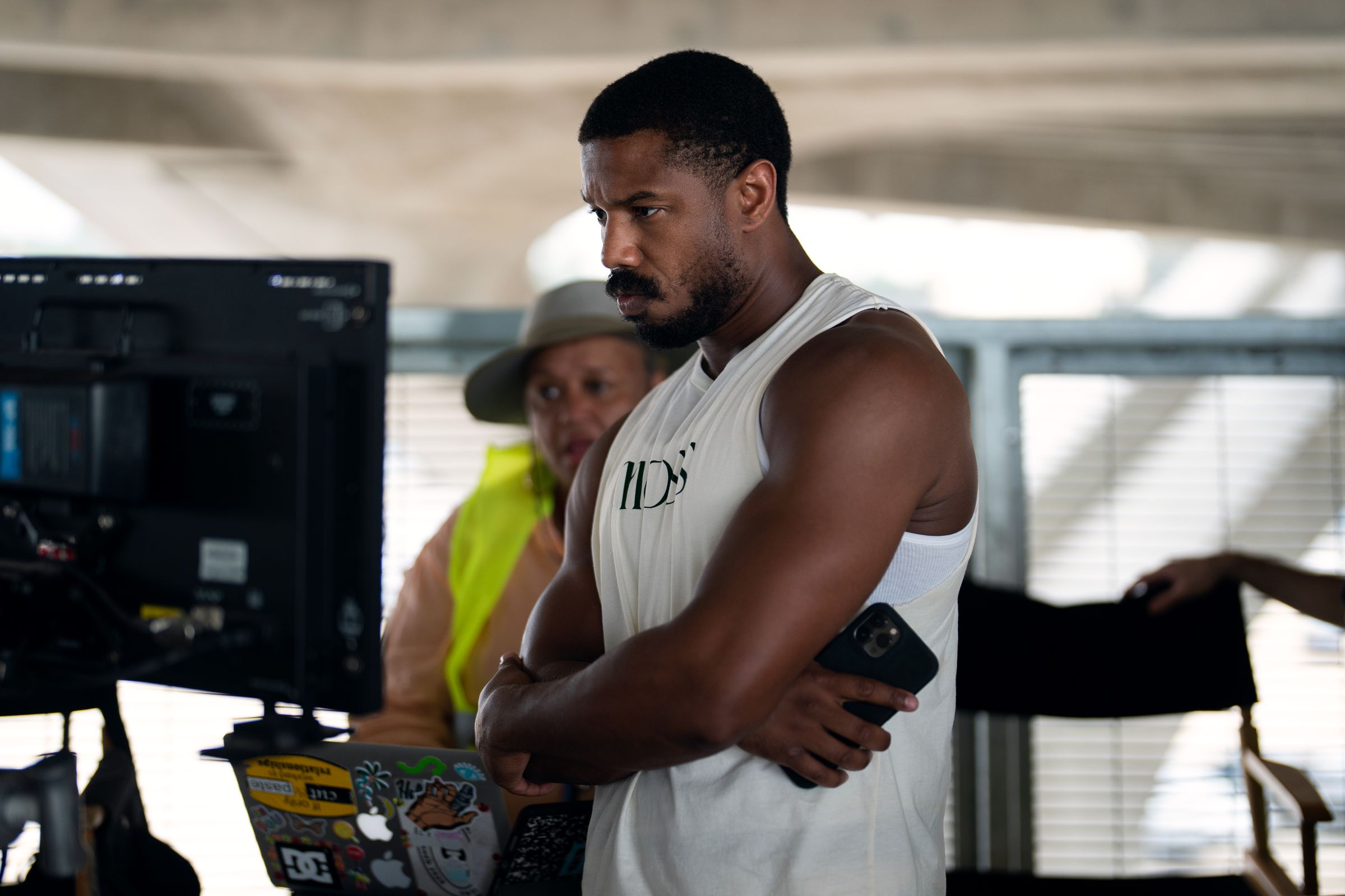 A man in a tank top looking at a monitor on a film set.