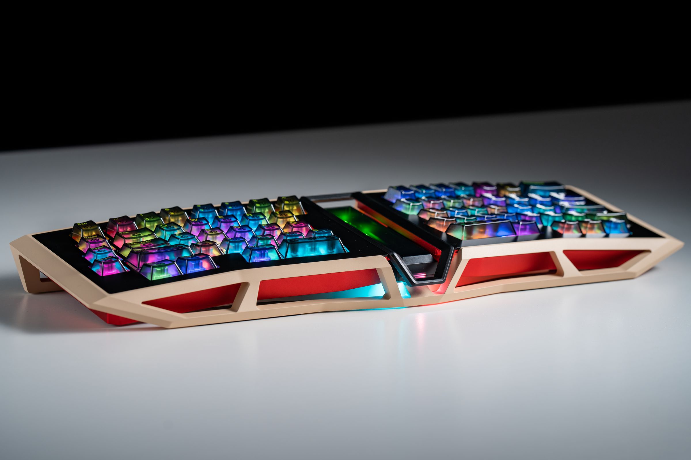 A tan and red ergonomic keyboard with see-through keycaps illuminated by multicolored light, resting on a white table.