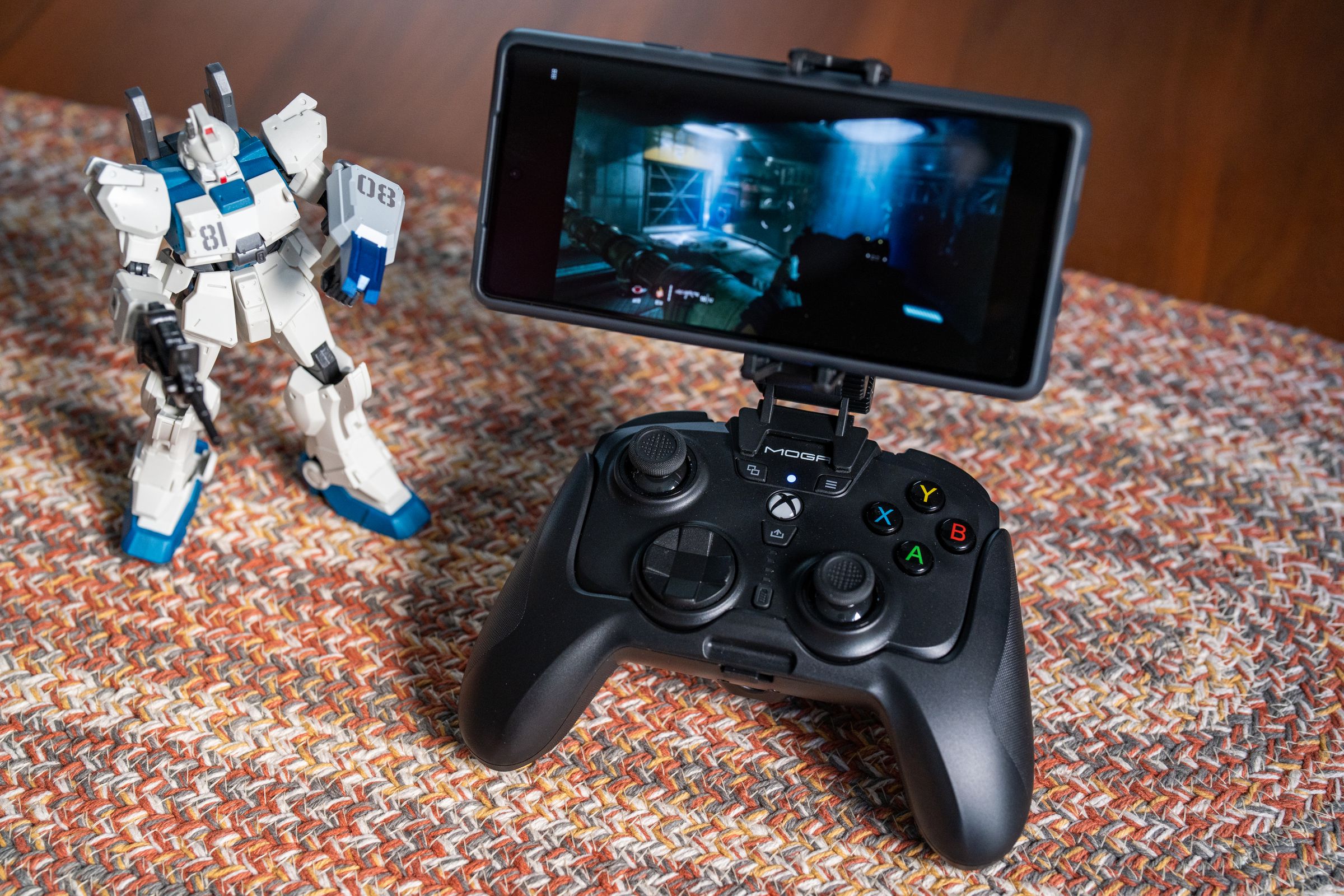 The PowerA MOGA XP-Ultra controller with a phone attached in its clip, sitting beside a Gundam figure.