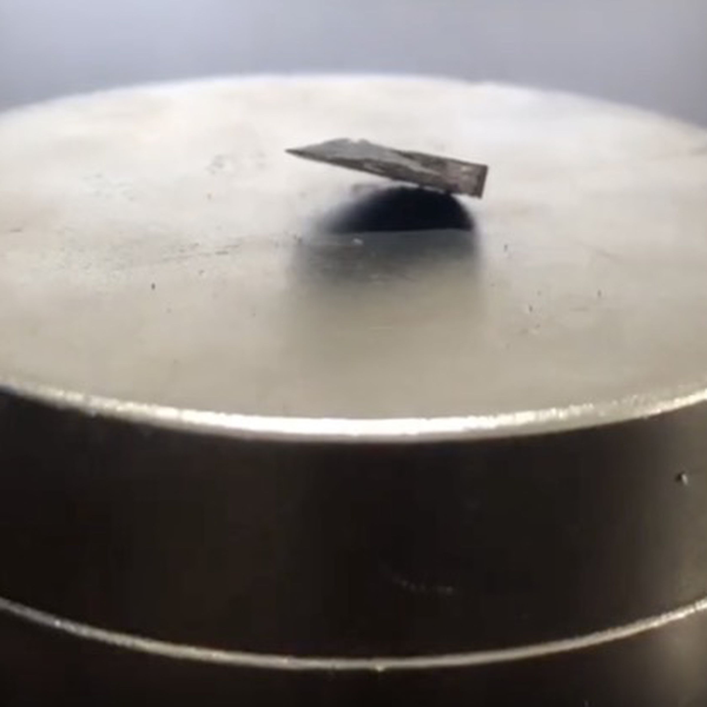 A piece of metal partially hovers above a magnet.