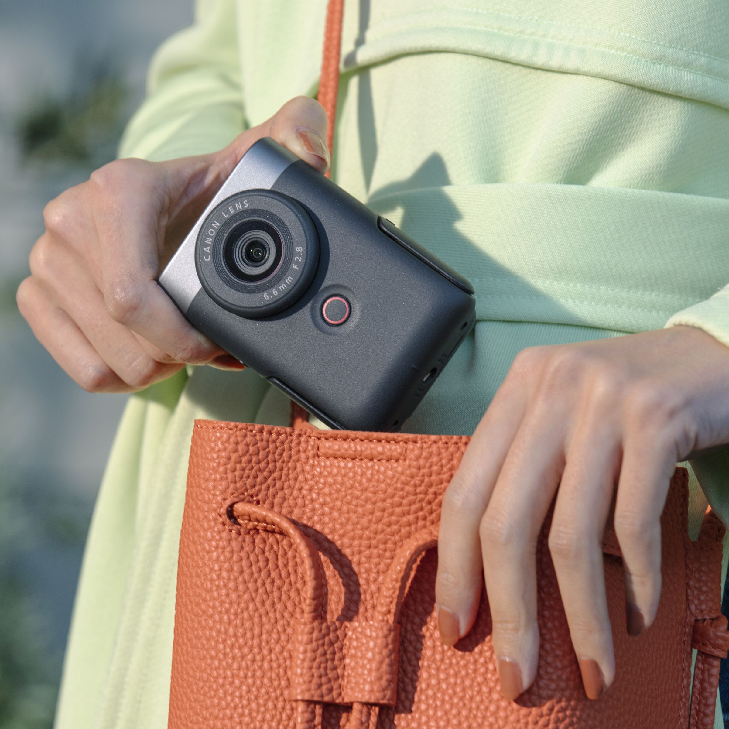 A person removing the Canon PowerShot V10 vlogging camera from an orange handbag.