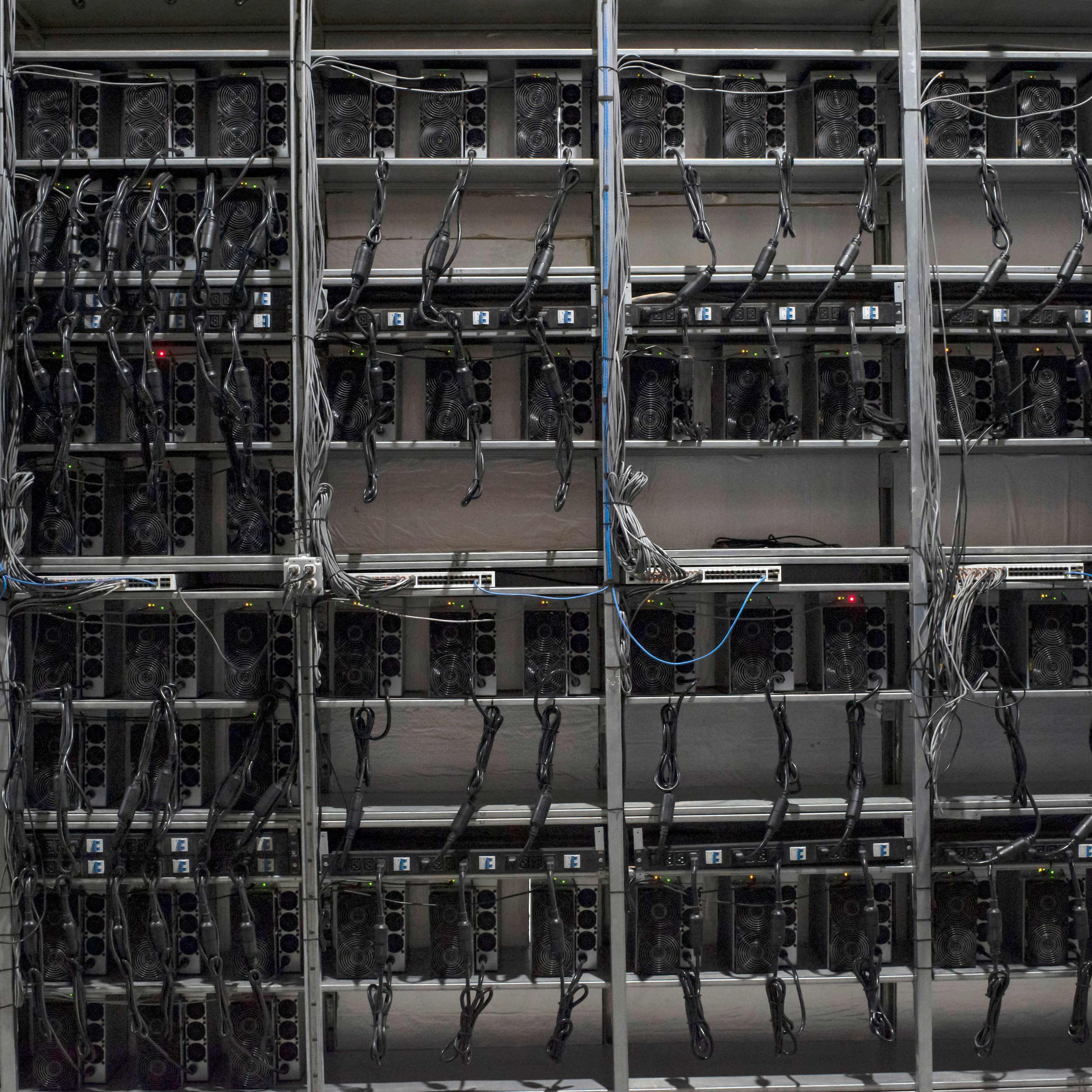 Rows of Bitcoin mining machines on shelves with wires hanging from them