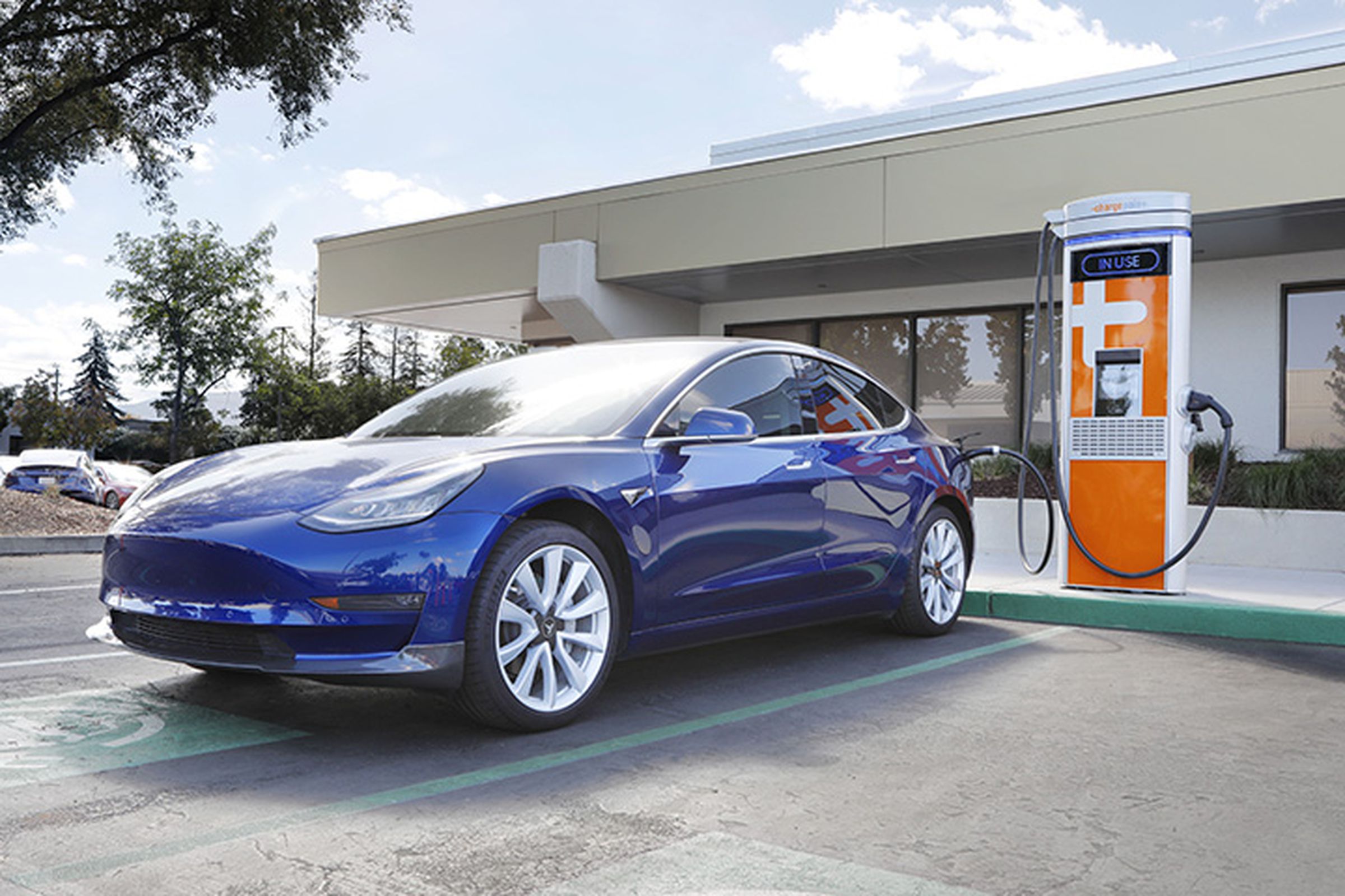 A photo of a Tesla parked in front of an orange charger.
