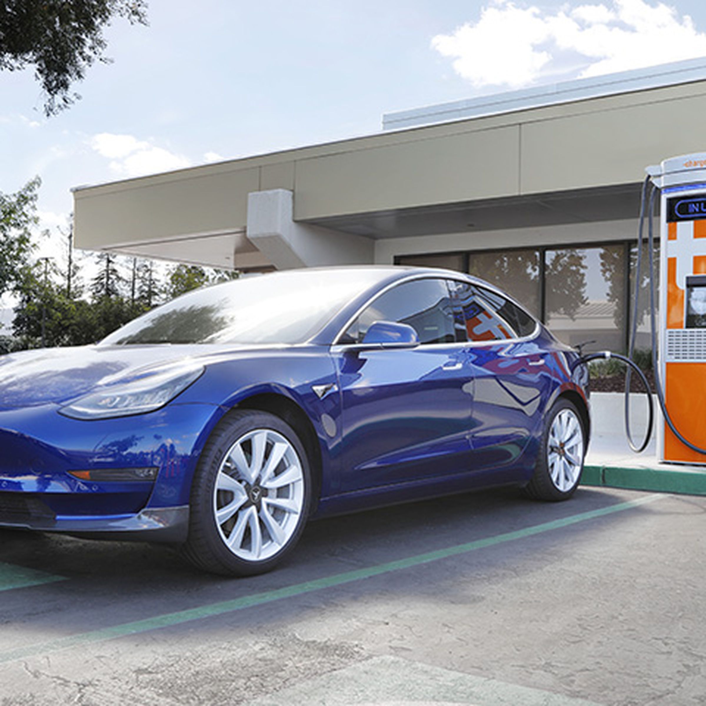 A photo of a Tesla parked in front of an orange charger.