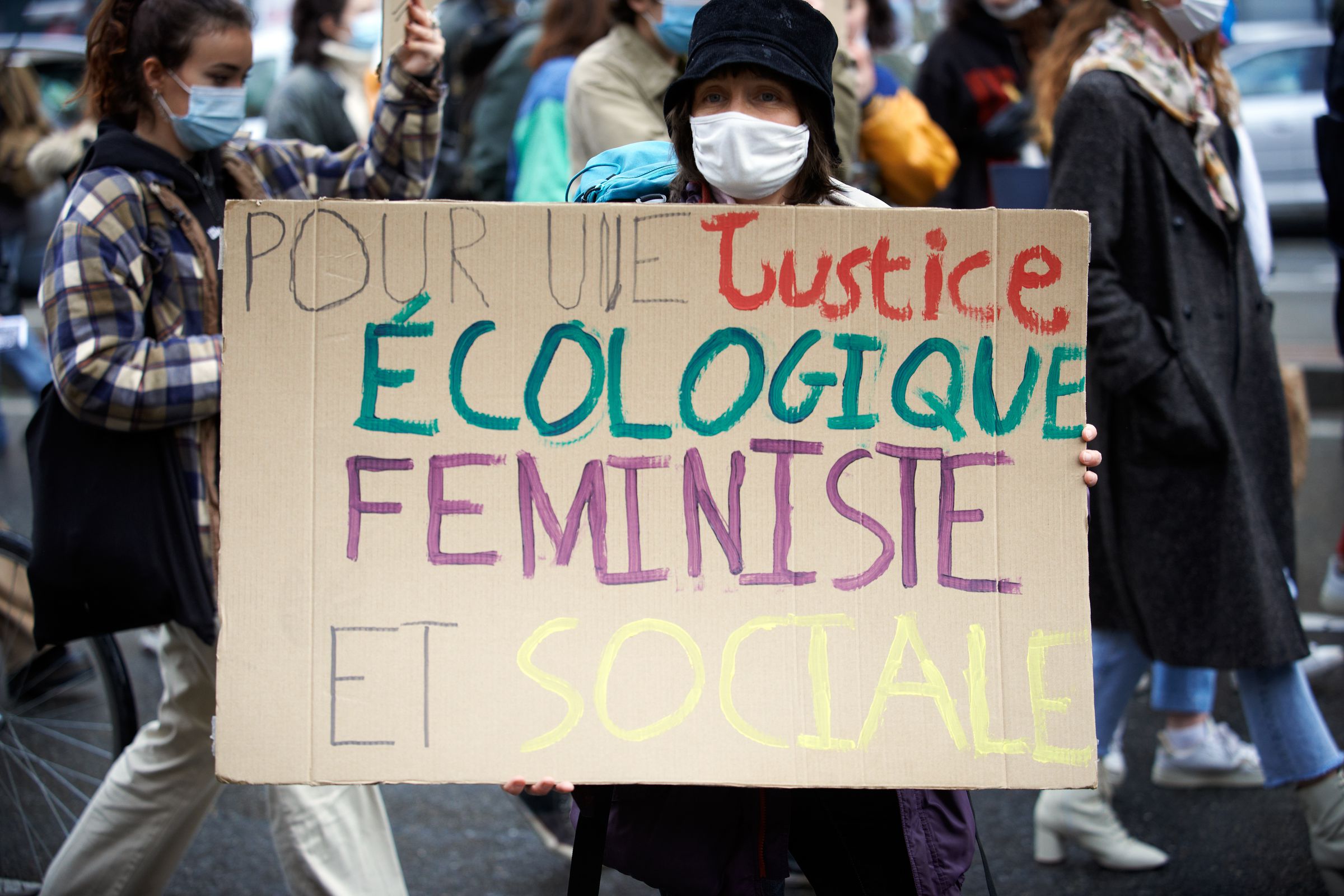 A person holds a cardboard sign with a message written in French that says, “Pour une justice ecologique feministe et sociale.”