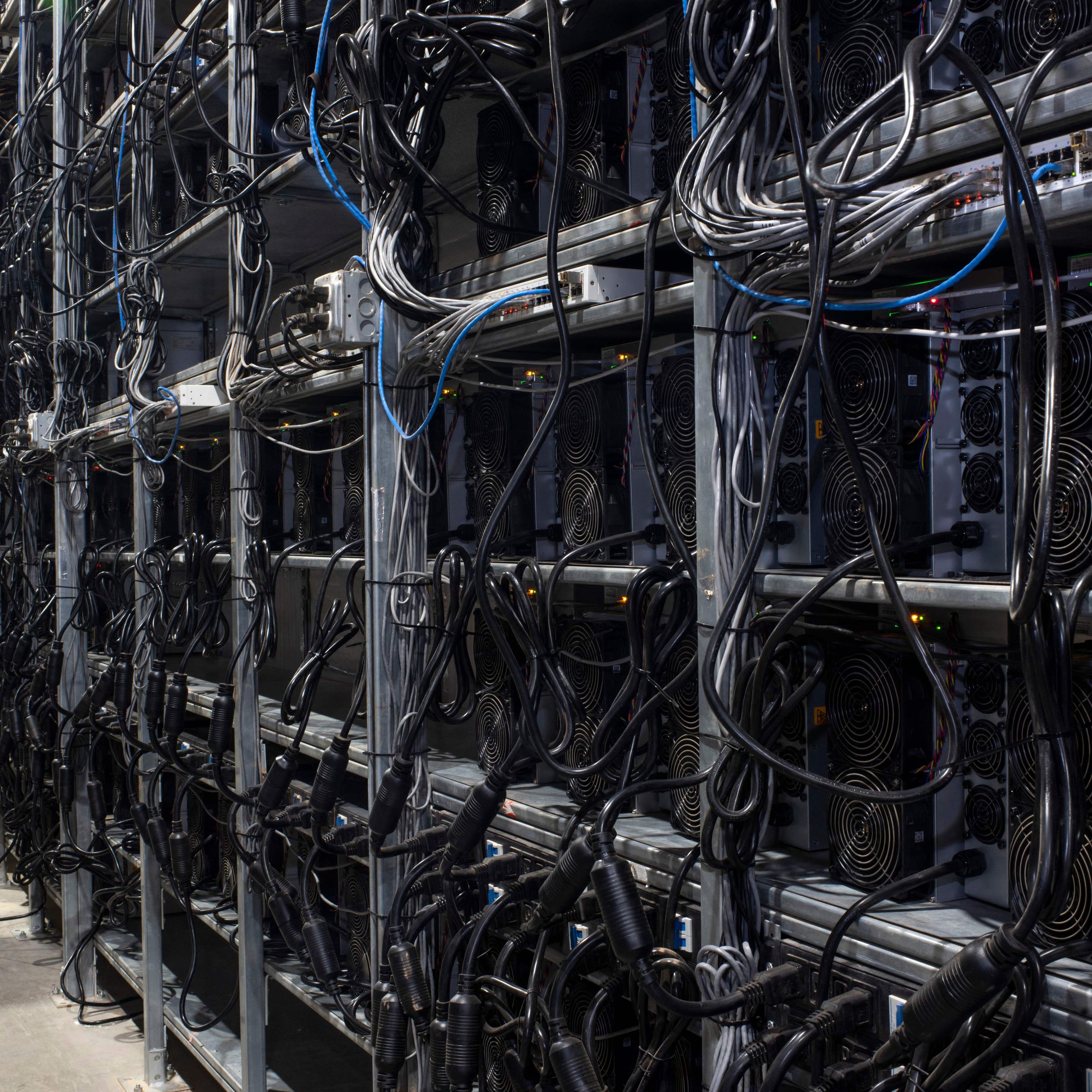 Racks of Bitcoin mining machines with wires hanging from them.