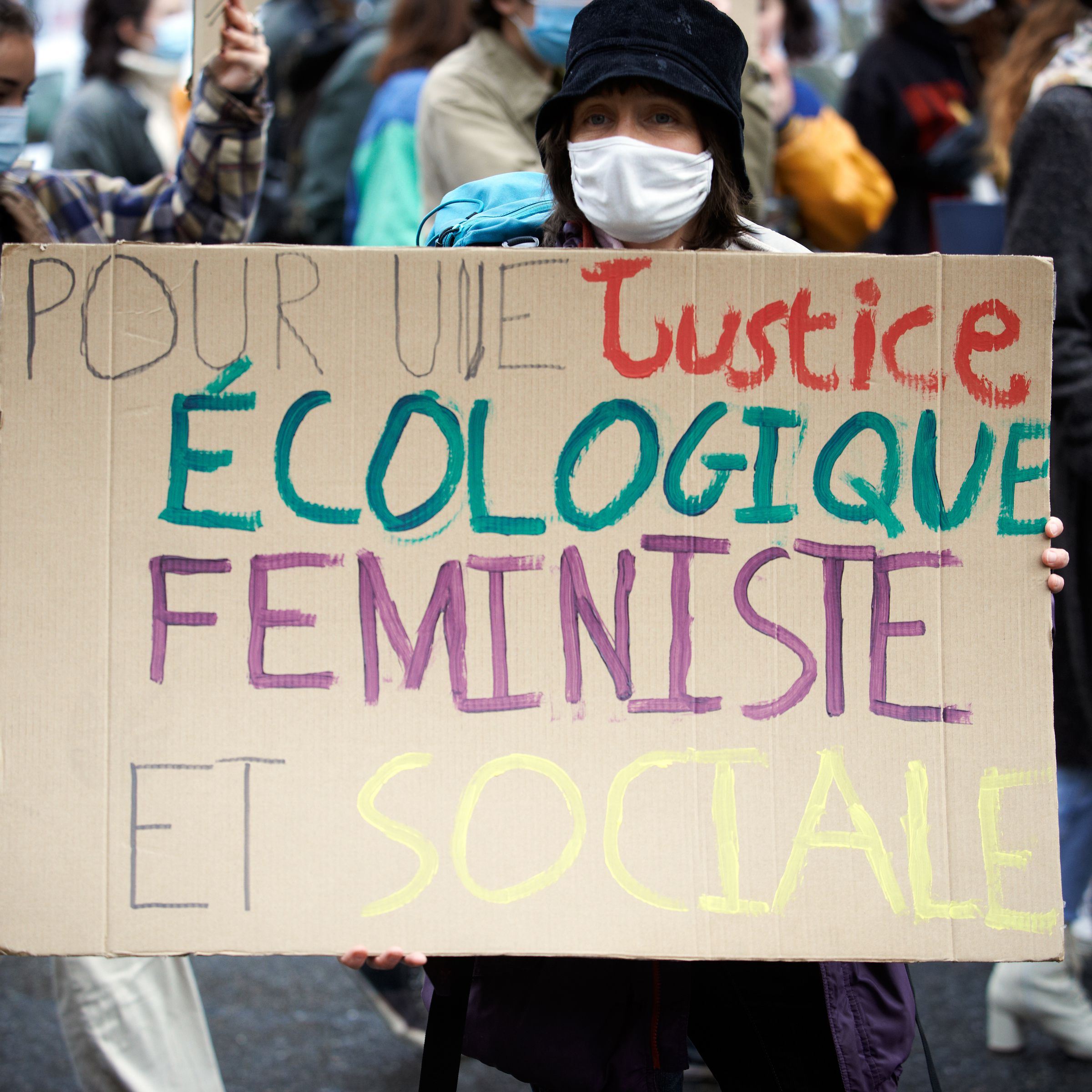 A person holds a cardboard sign with a message written in French that says, “Pour une justice ecologique feministe et sociale.”