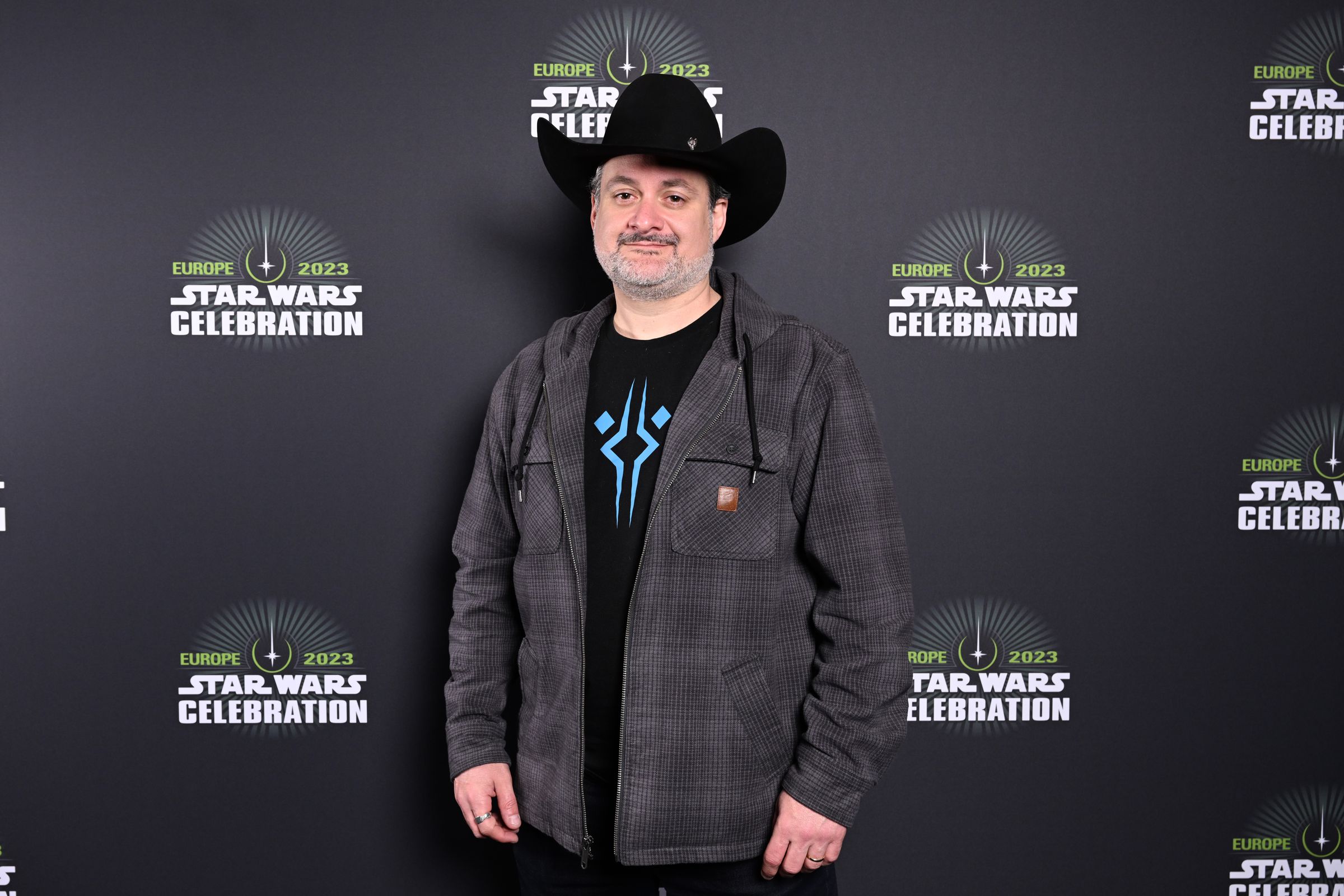 Dave Filoni in front of a Star Wars Celebration backdrop. He’s wearing a cowboy hat, yeehaw.