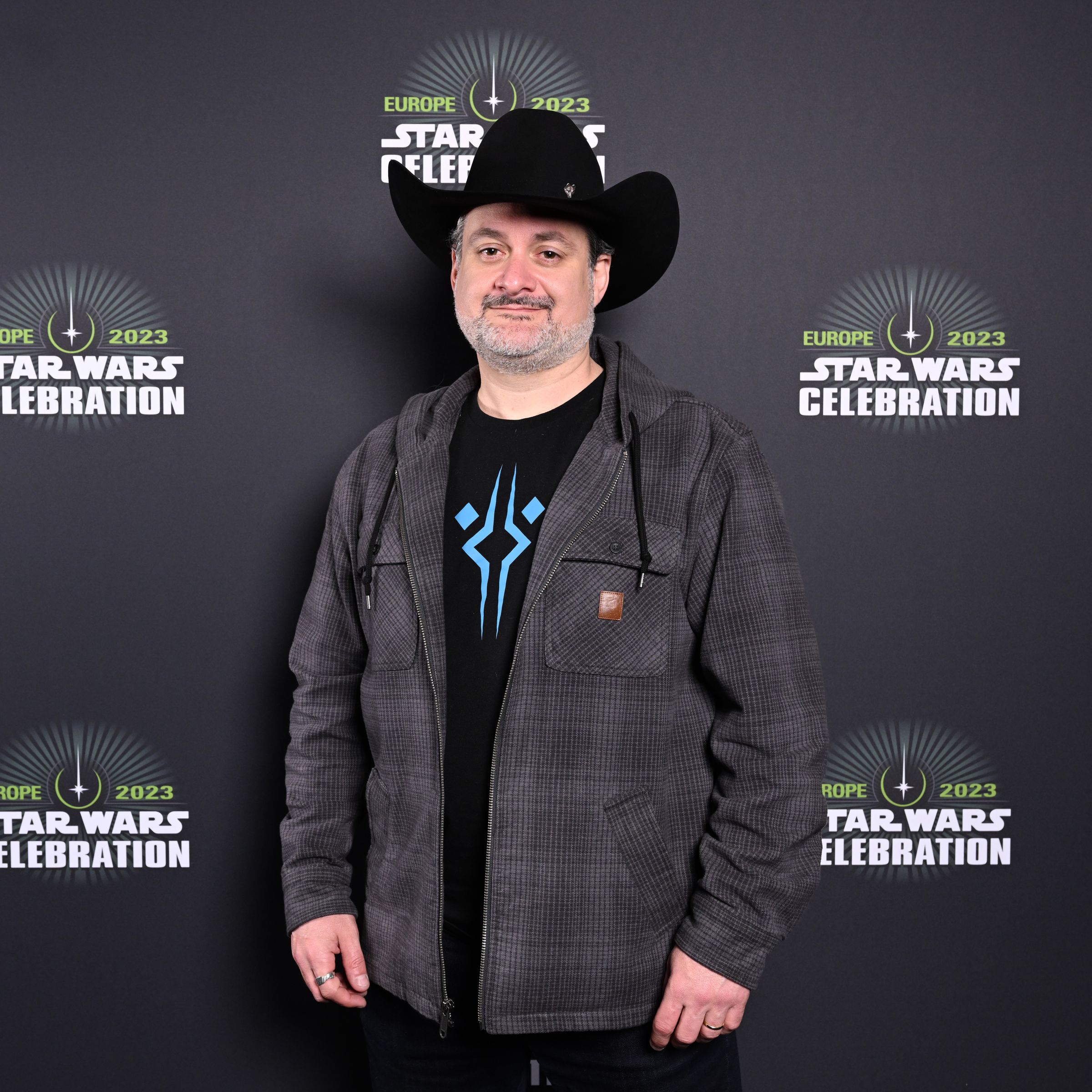 Dave Filoni in front of a Star Wars Celebration backdrop. He’s wearing a cowboy hat, yeehaw.