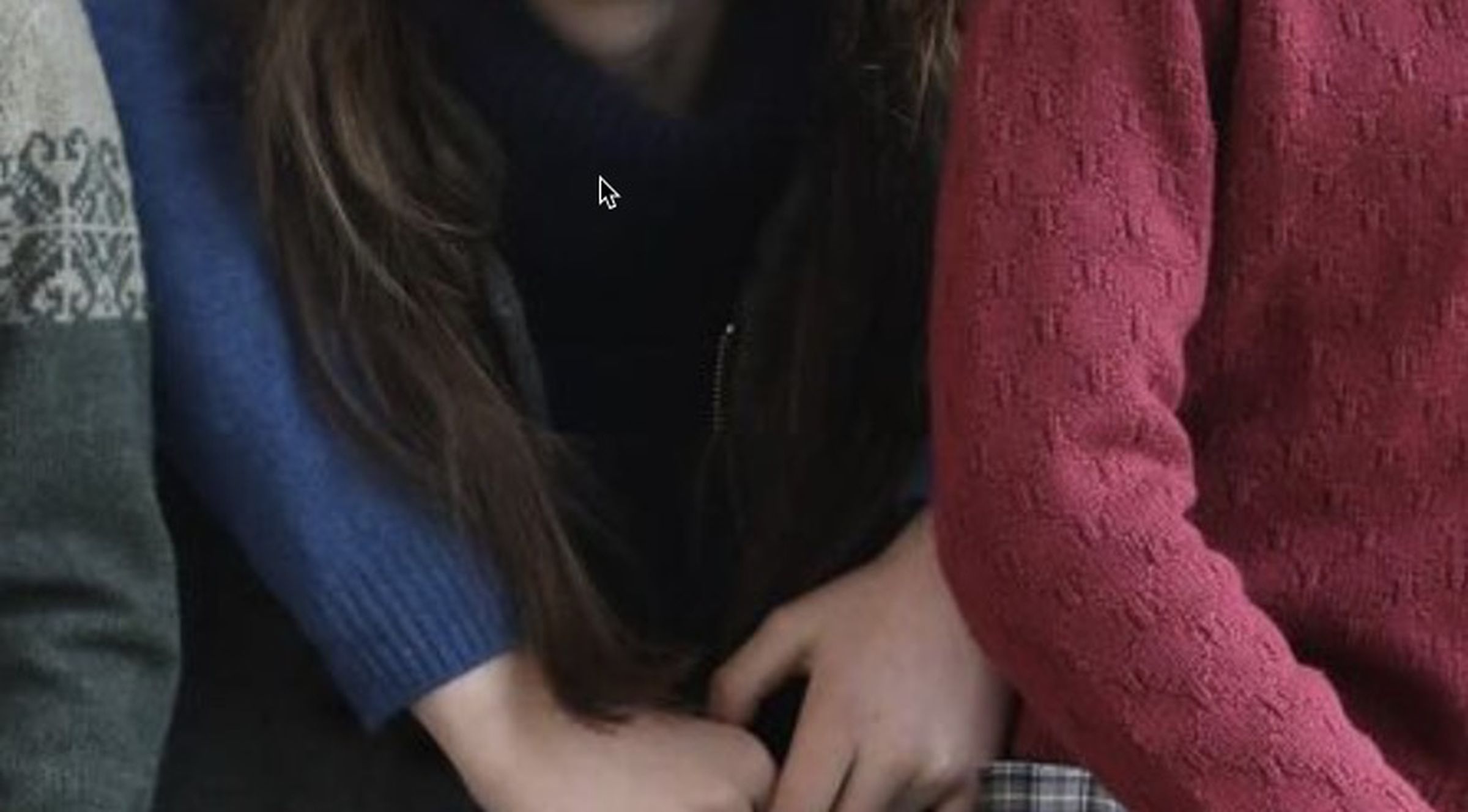 An image of a woman’s hair atop a boy’s sweater, the shadows are so dense as to suggest they are not real.