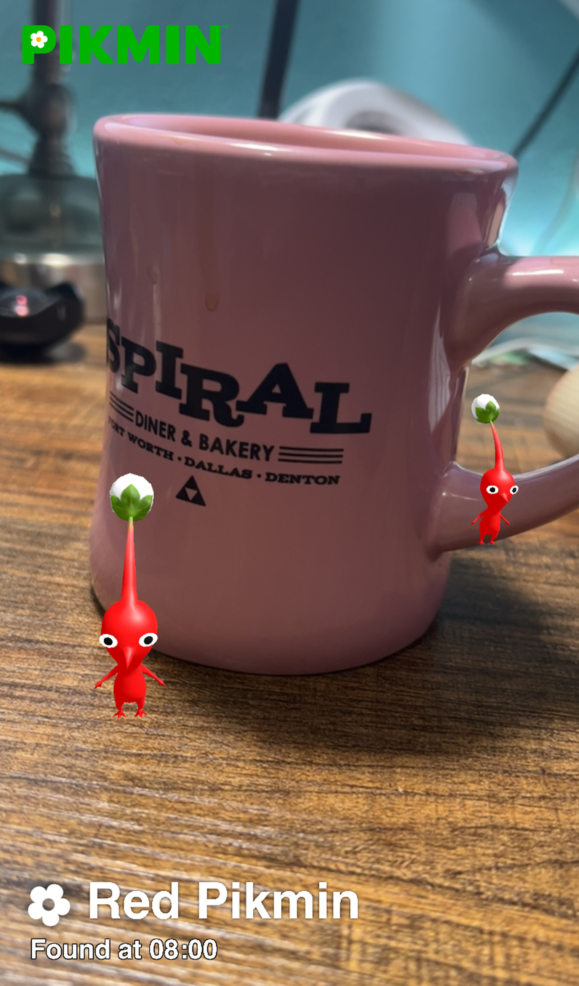 A picture of two pikmin standing around a pink diner-style coffee mug.