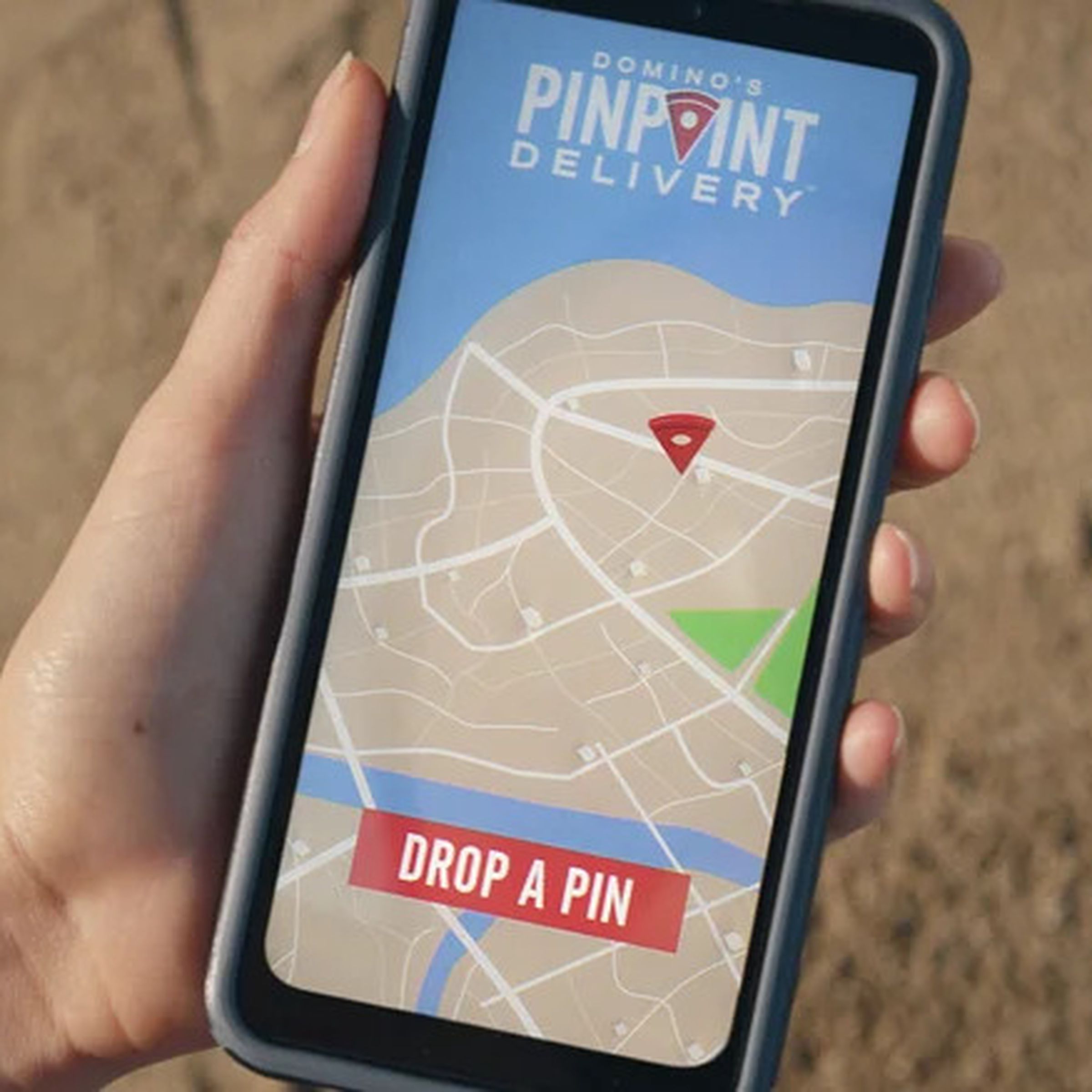 A hand holding a smartphone opened to the Domino’s app, with the “Pinpoint Delivery” ordering page visible.