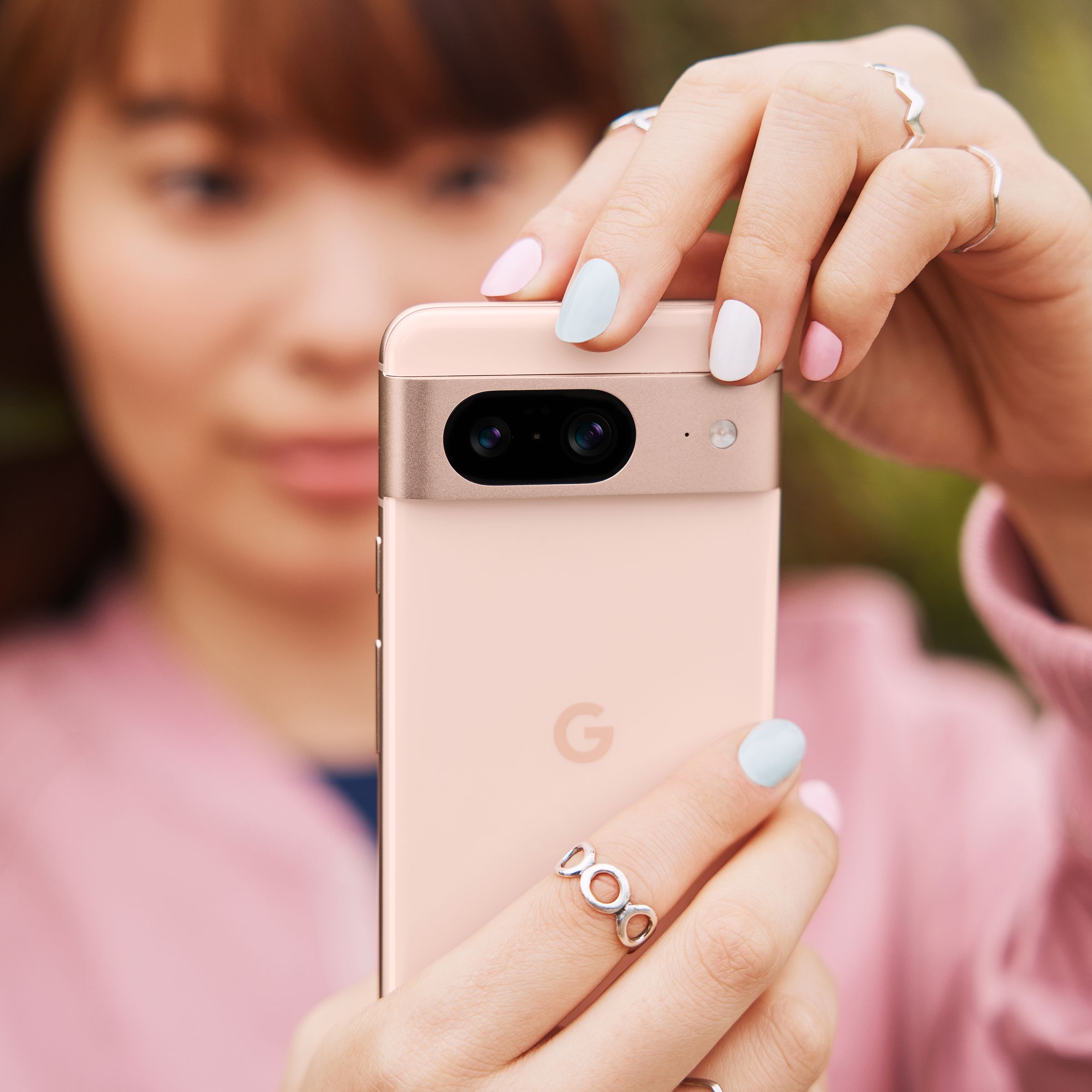 A young woman taking a photo with a rose pink Pixel 8.