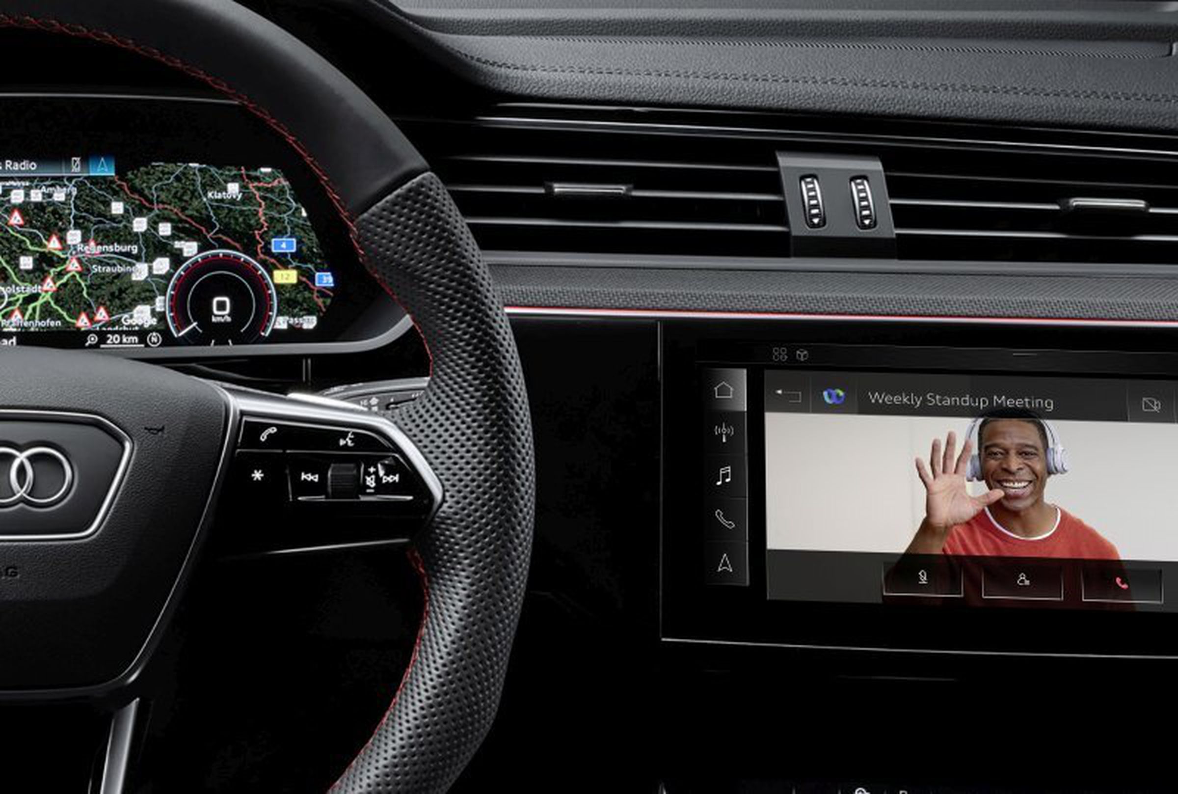 interior of Audi vehicle showing steering wheel, dash, and infotainment screen with man waving hand on the screen.