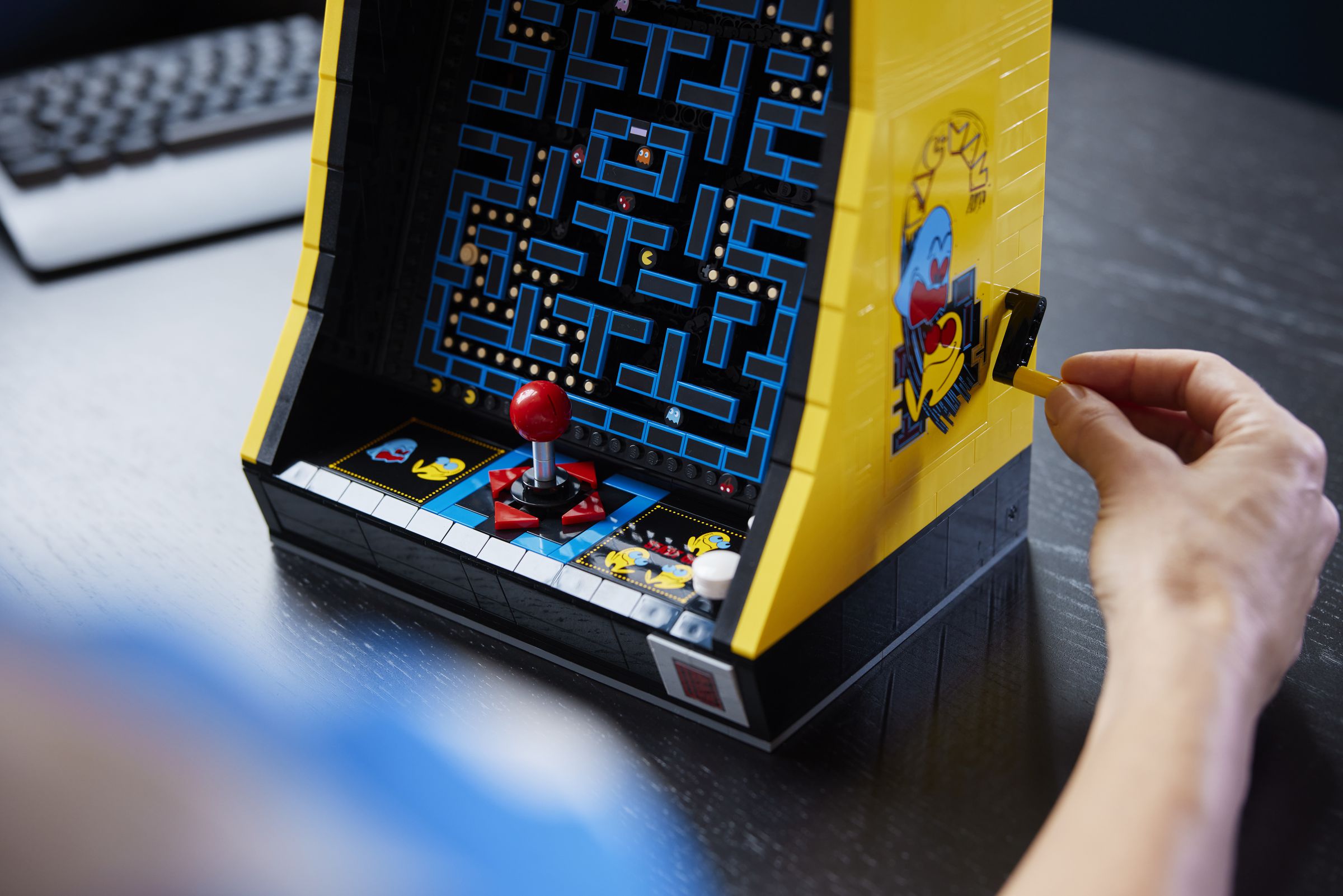 A person turns the crank on the side of the lego arcade cabinet.