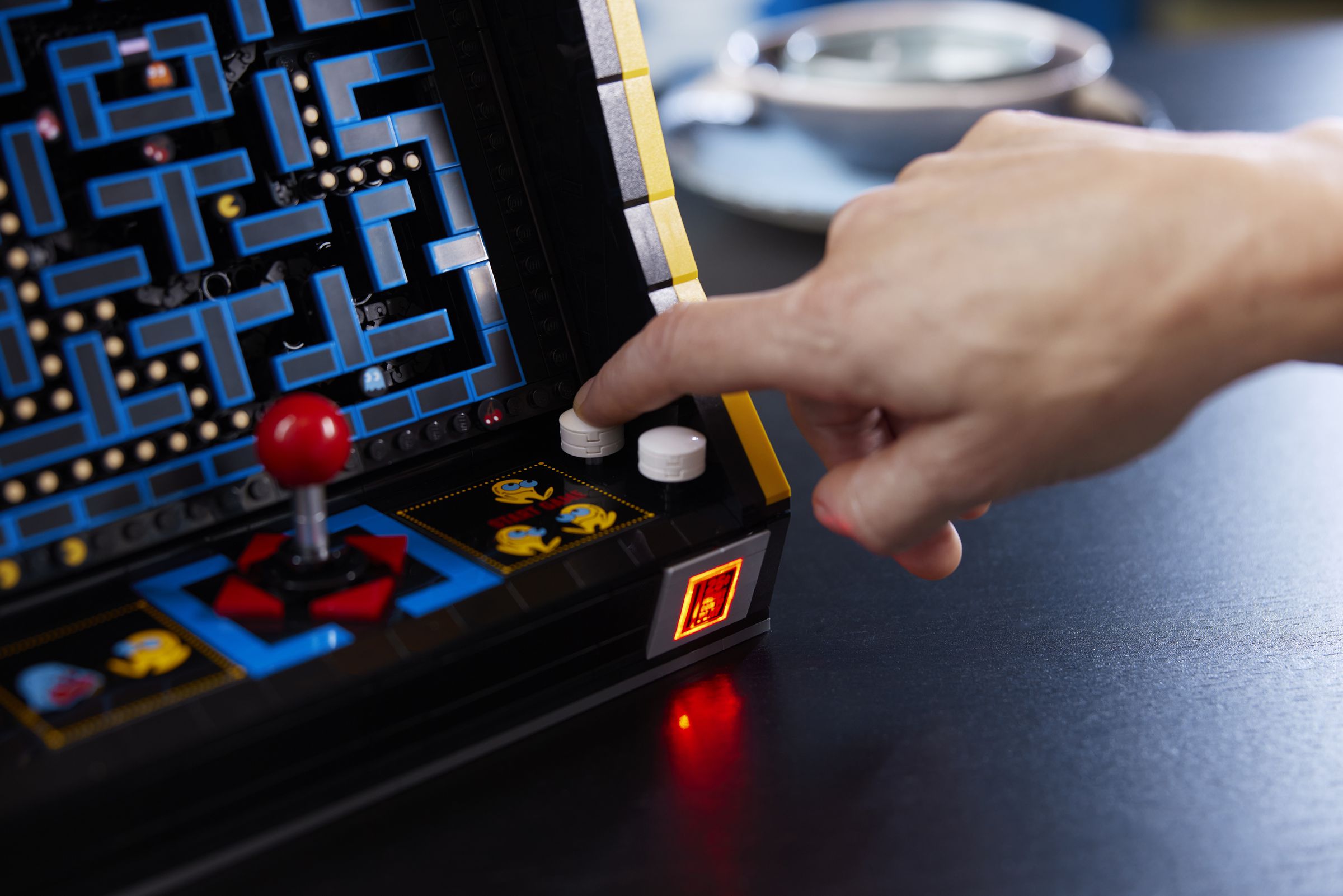 A person presses a button on the arcade cabinet, causing its coin-slot to light up.