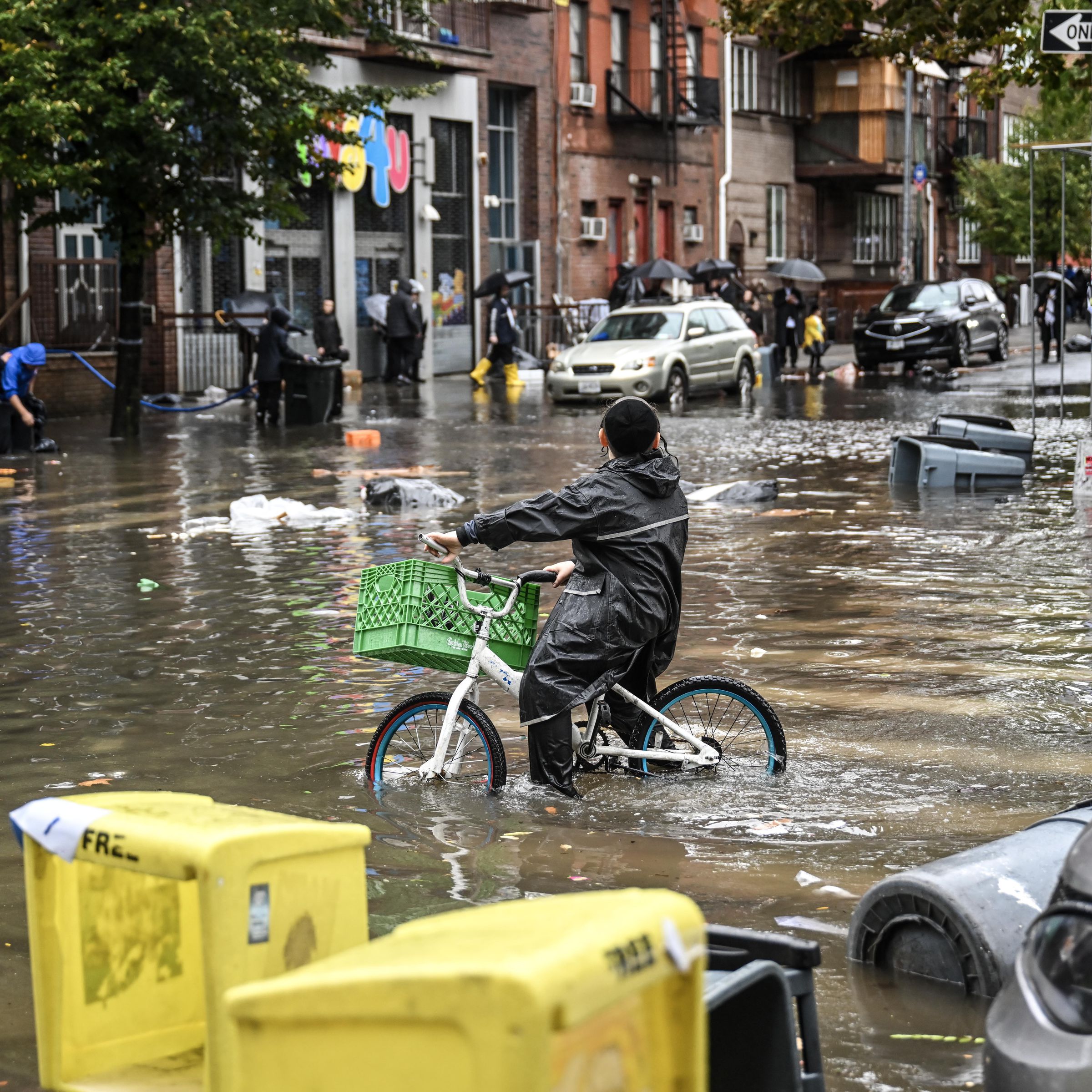A biker and several pedestrians wade through a flooded street.