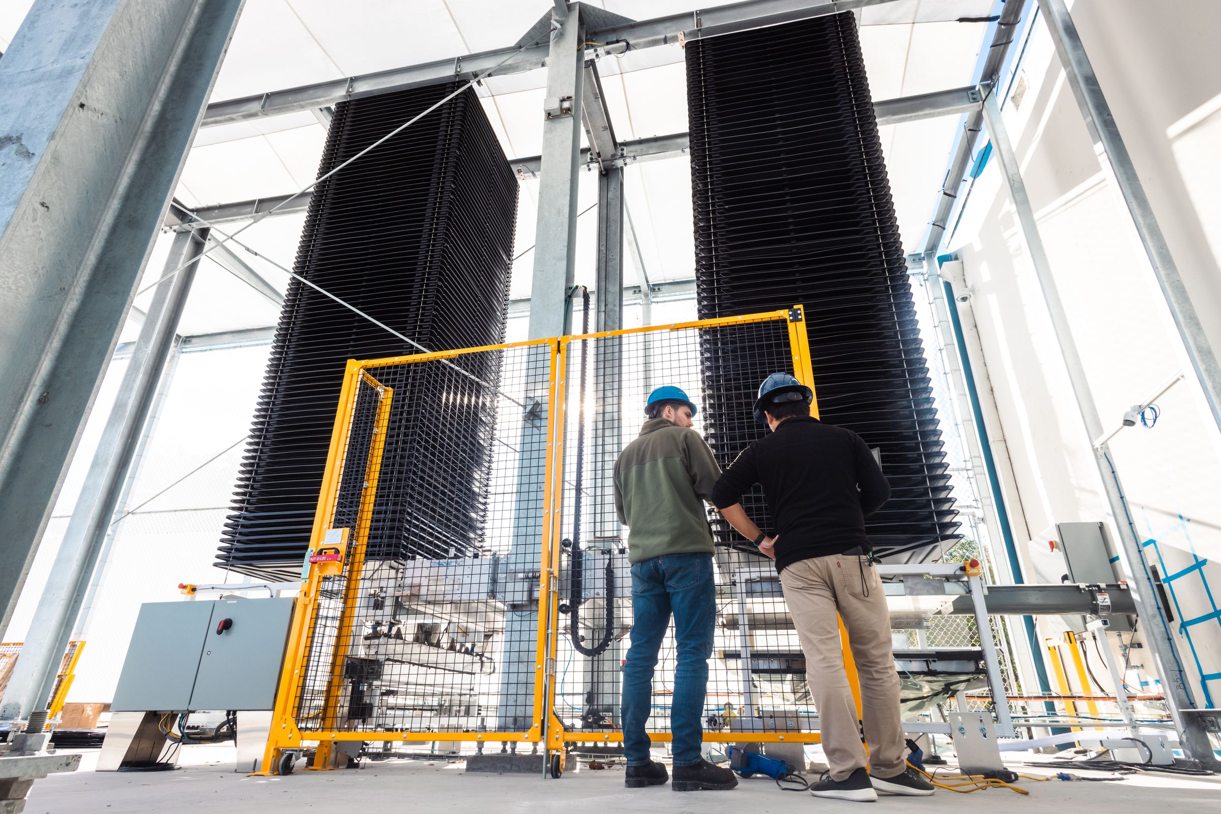 Two men wearing hard hats stand in front of rectangular stacks filtering CO2 out of the air