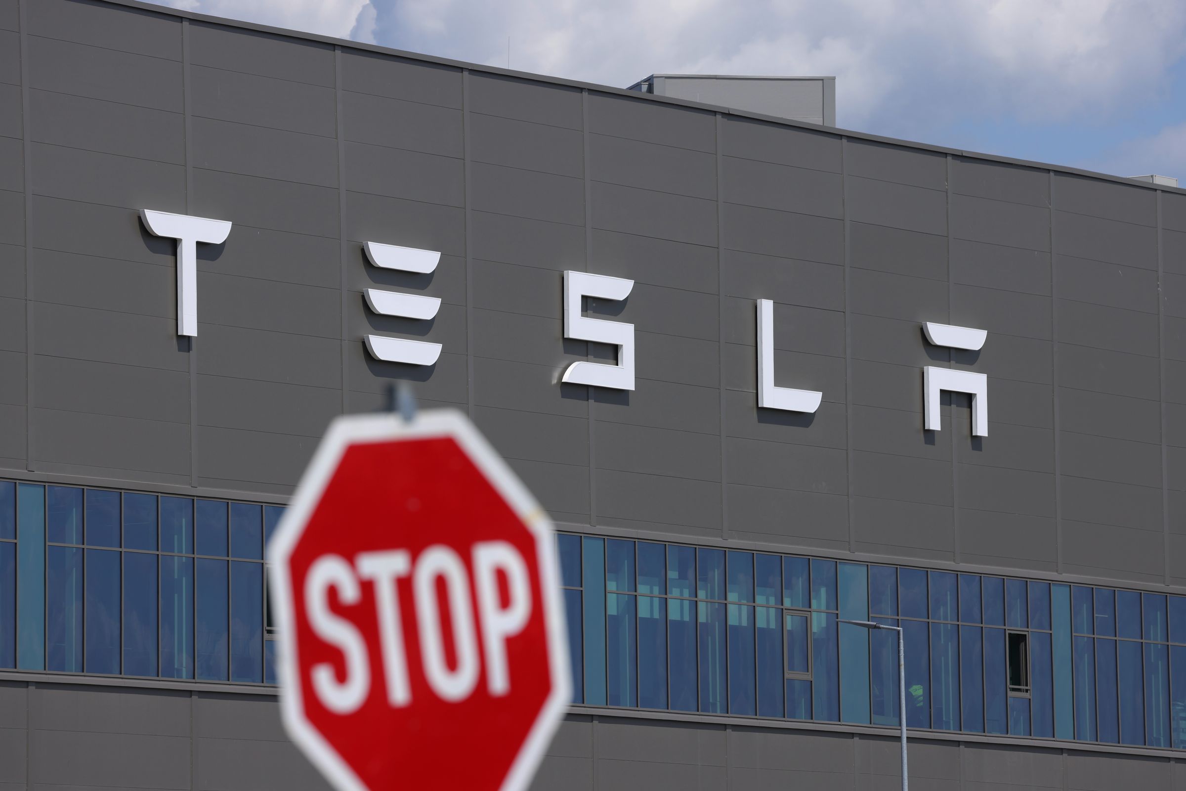 A stop sign stands near the Tesla logo at the Tesla factory on July 17th, 2023, near Gruenheide, Germany.