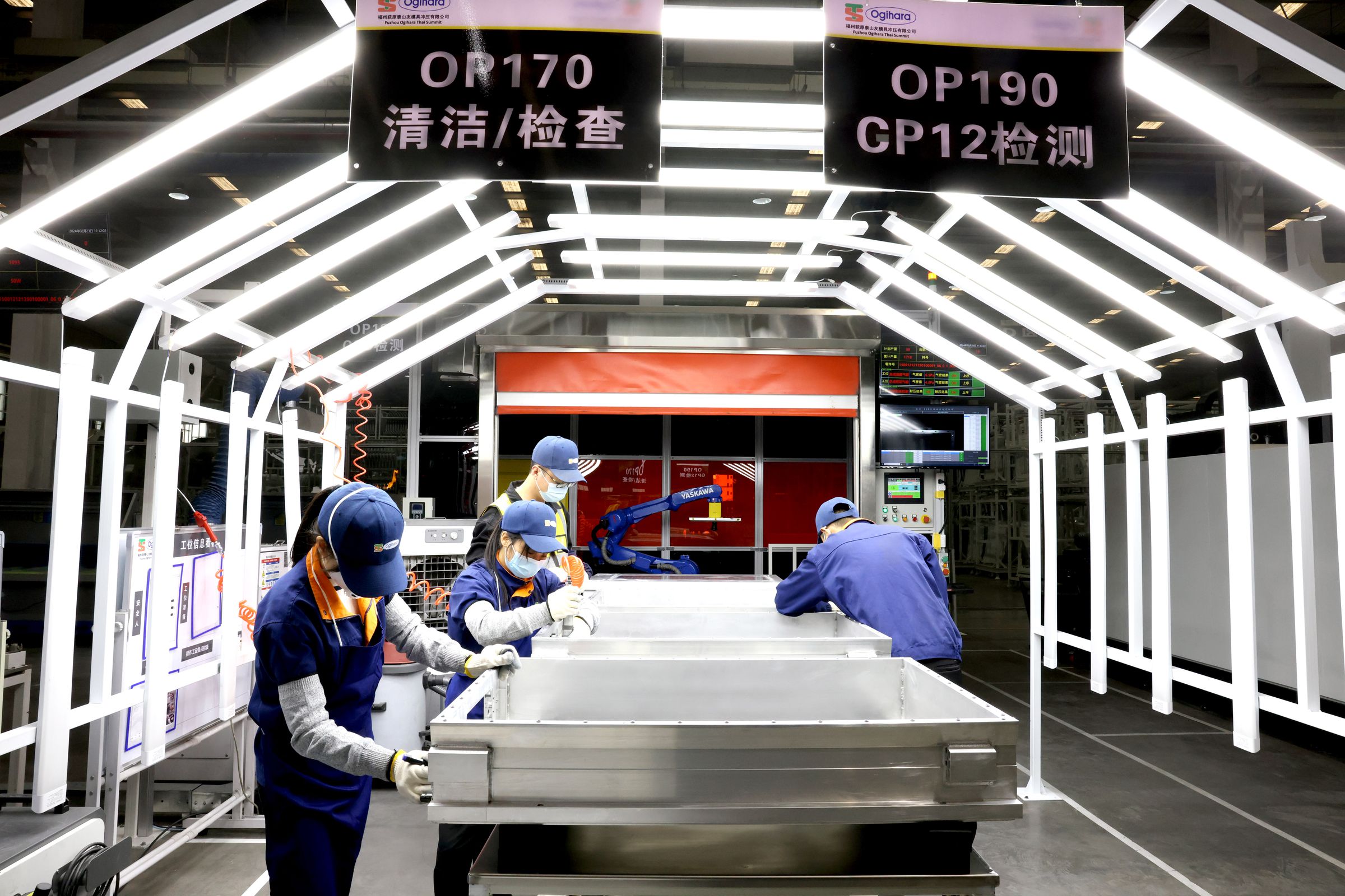 Four workers standing at a battery assembly line.