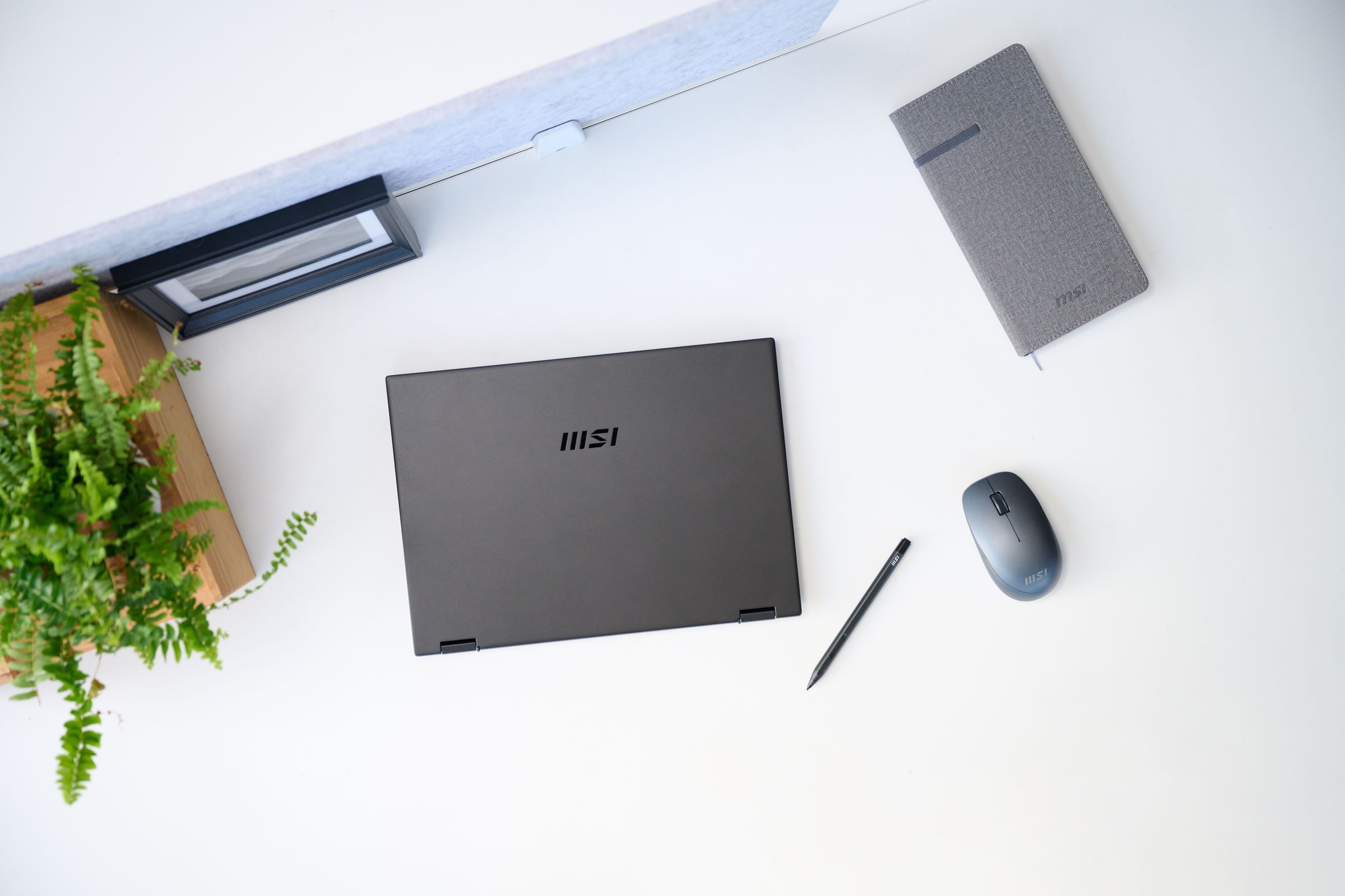 The MSI Summit E14 Flip seen from above on a white table with an MSI-branded notebook, mouse and pen to its left and a houseplant to its right.