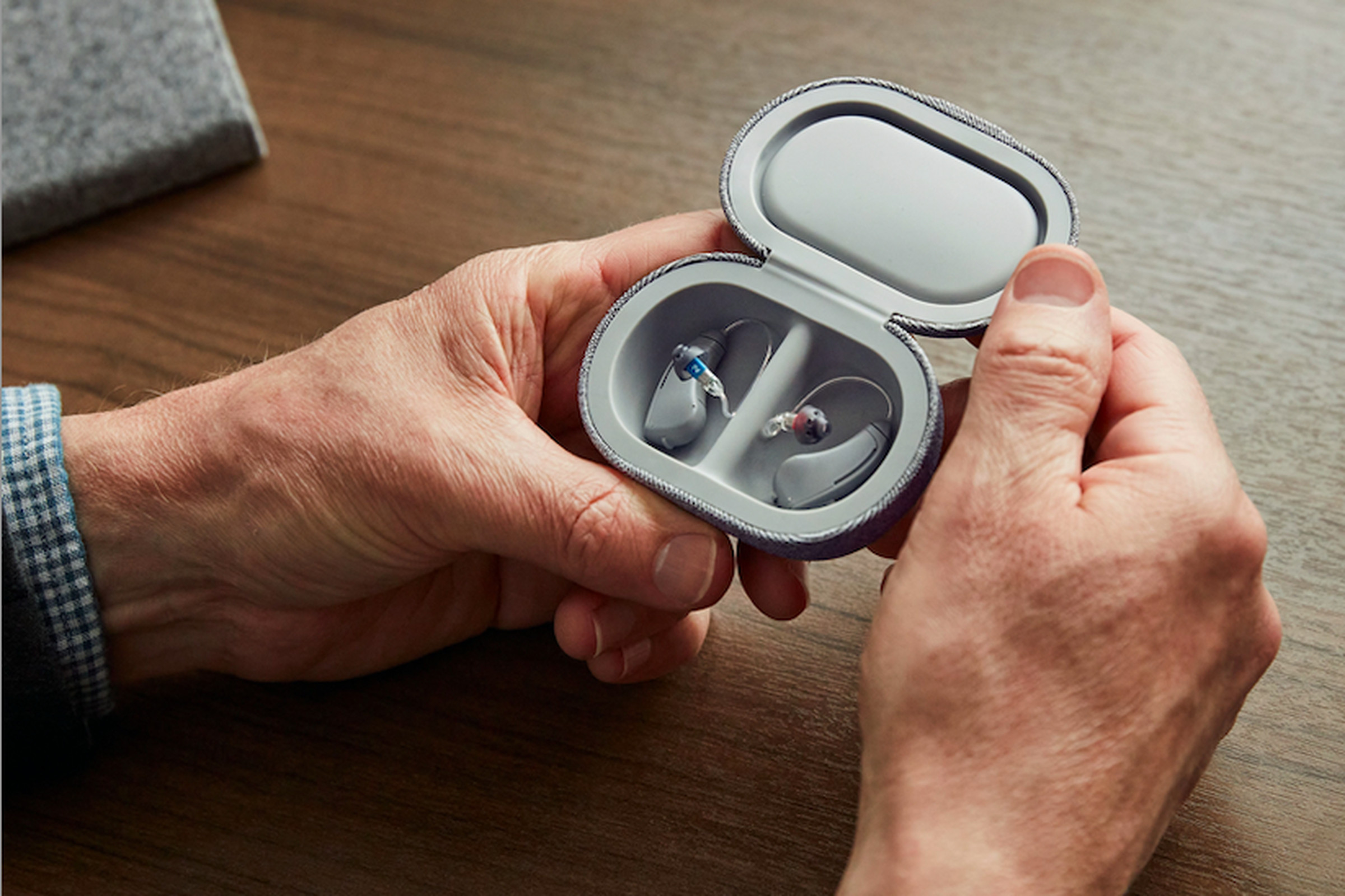 A pair of hands holding a small case with Bose hearing aids inside.