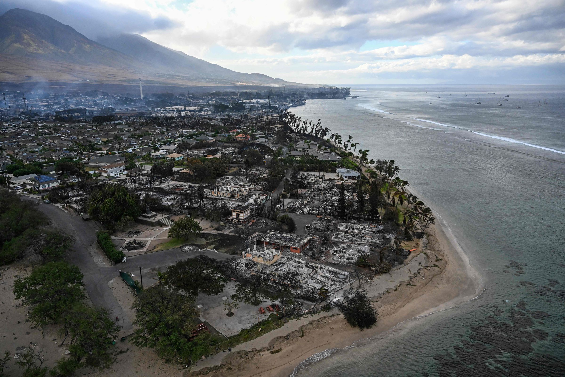 Smoke rises from remnants of burned homes and buildings in a community by the shoreline.