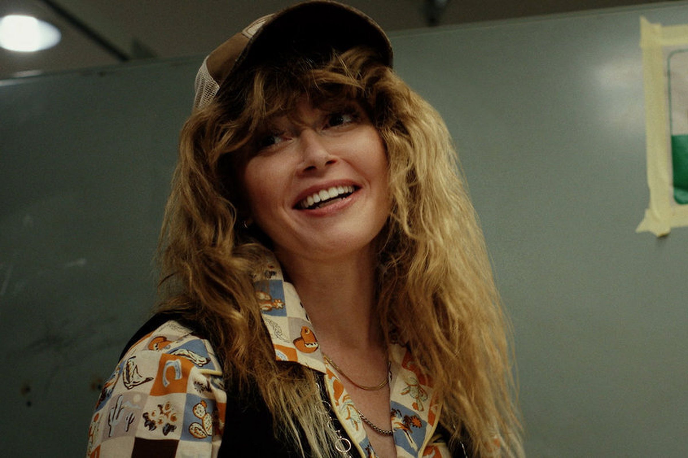 A woman in a hat, a blouse, and a vest, smiling.