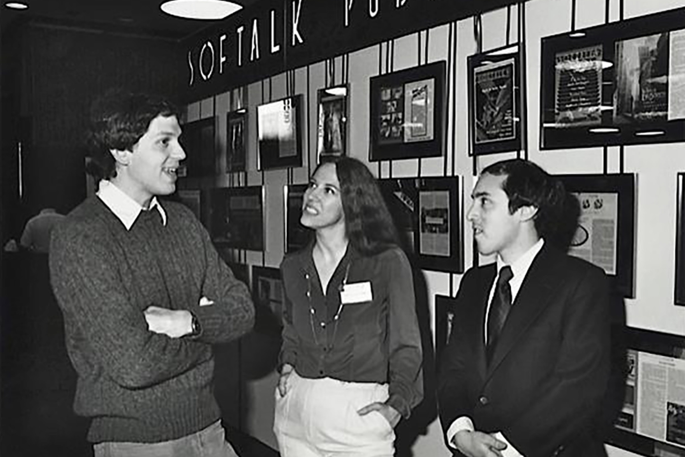Margot Comstock, dressed in a silk shirt and pale trouses, stands between two men, Marc Blank, and Joel Berez. The image is black and white.