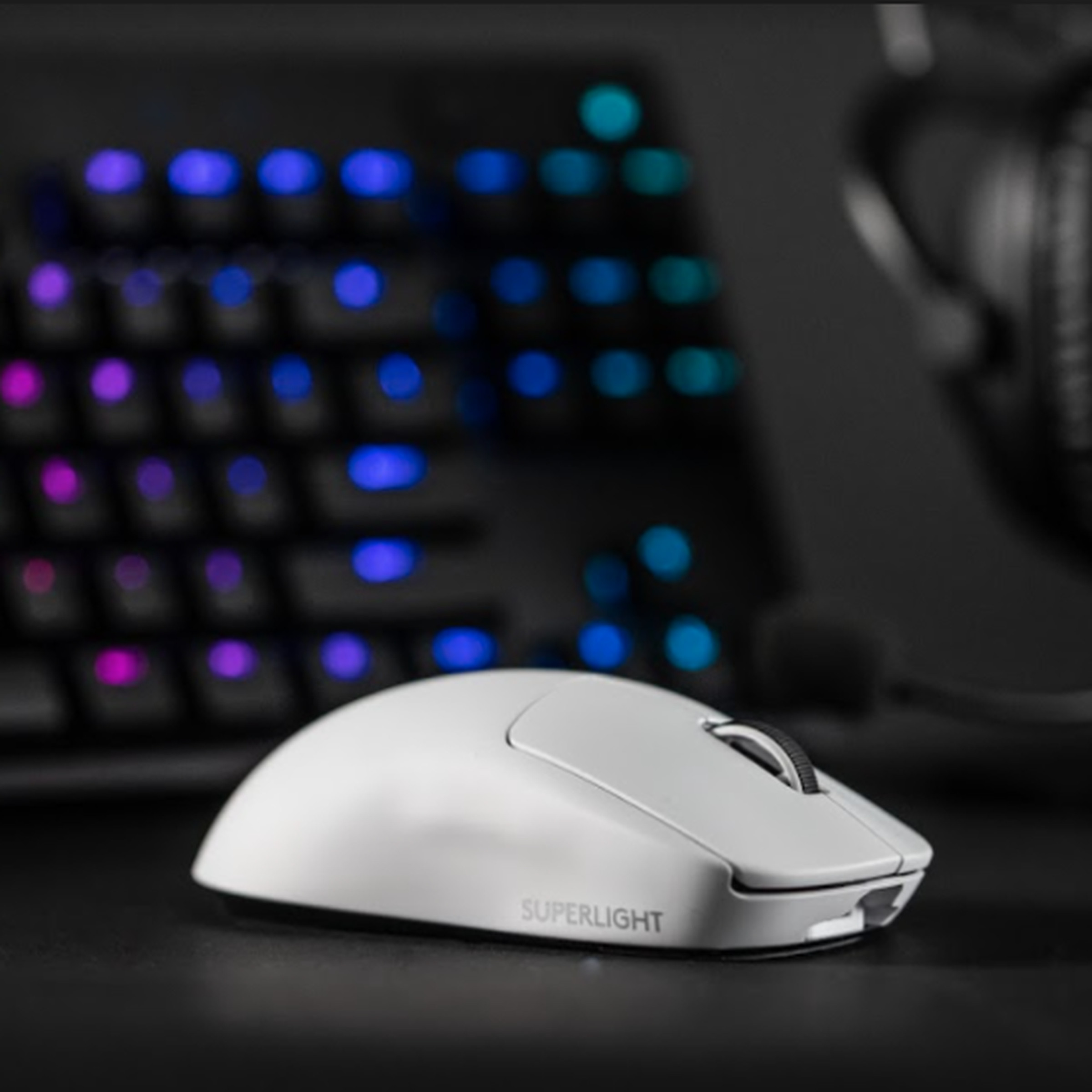 A close-up image of Logitech’s white G Pro X Superlight mouse in front of a headset and an RGB keyboard.