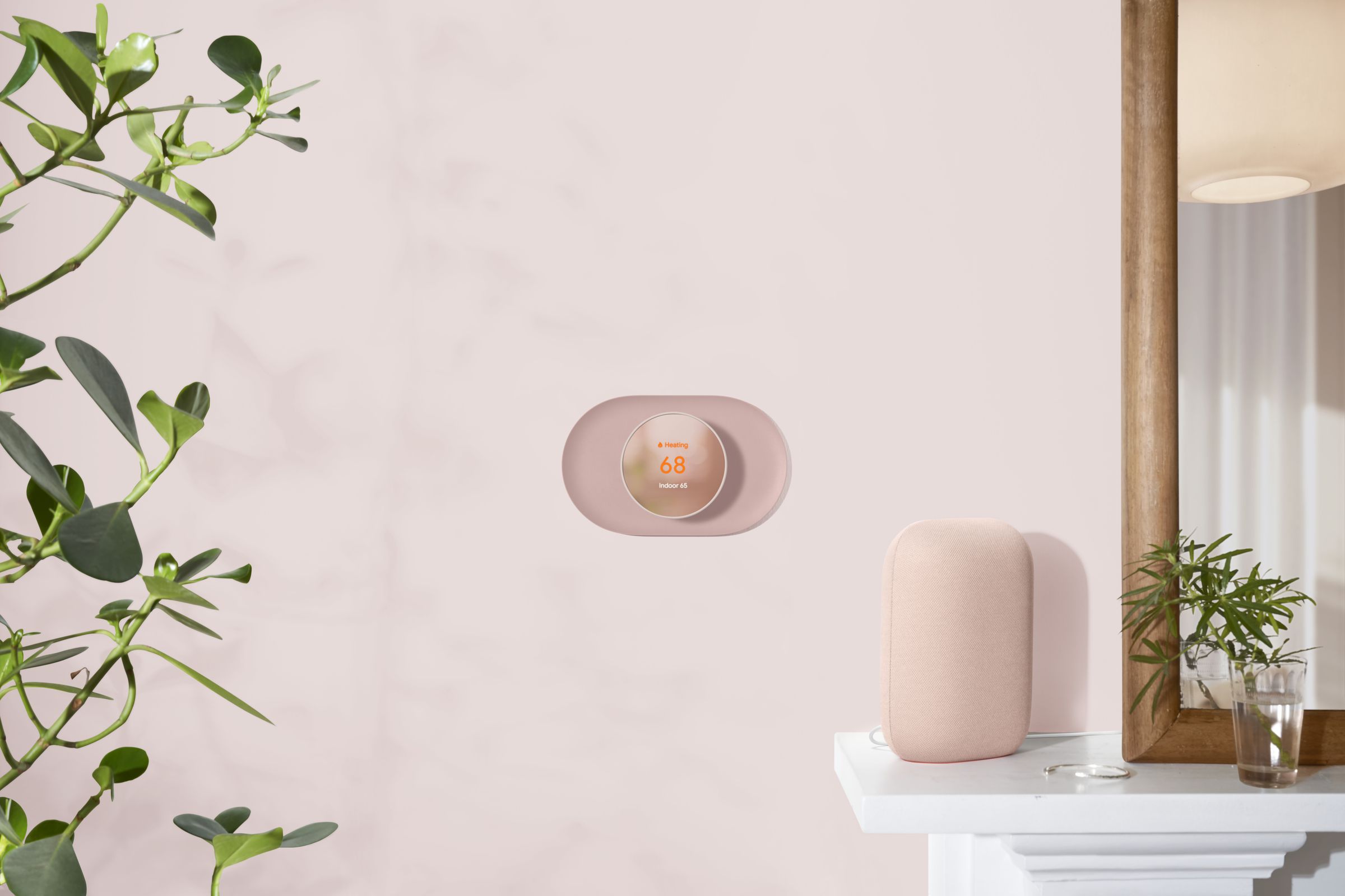A light pink Nest Thermostat mounted on the wall with a matching color Nest Audio speaker on a shelf next to it.