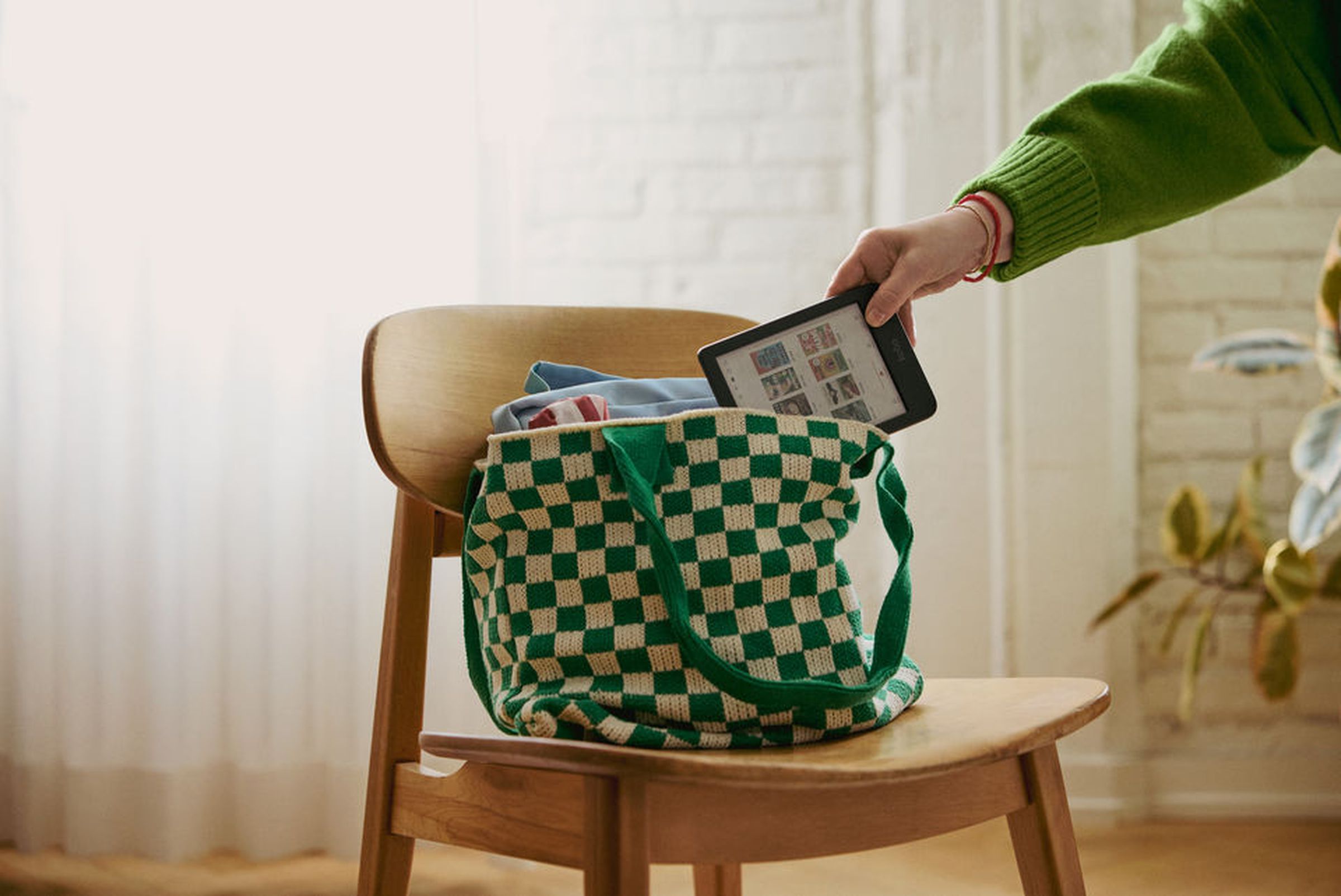 An image of an outstretched hand stuffing a Kobo Libra Colour into a green-and-white purse.