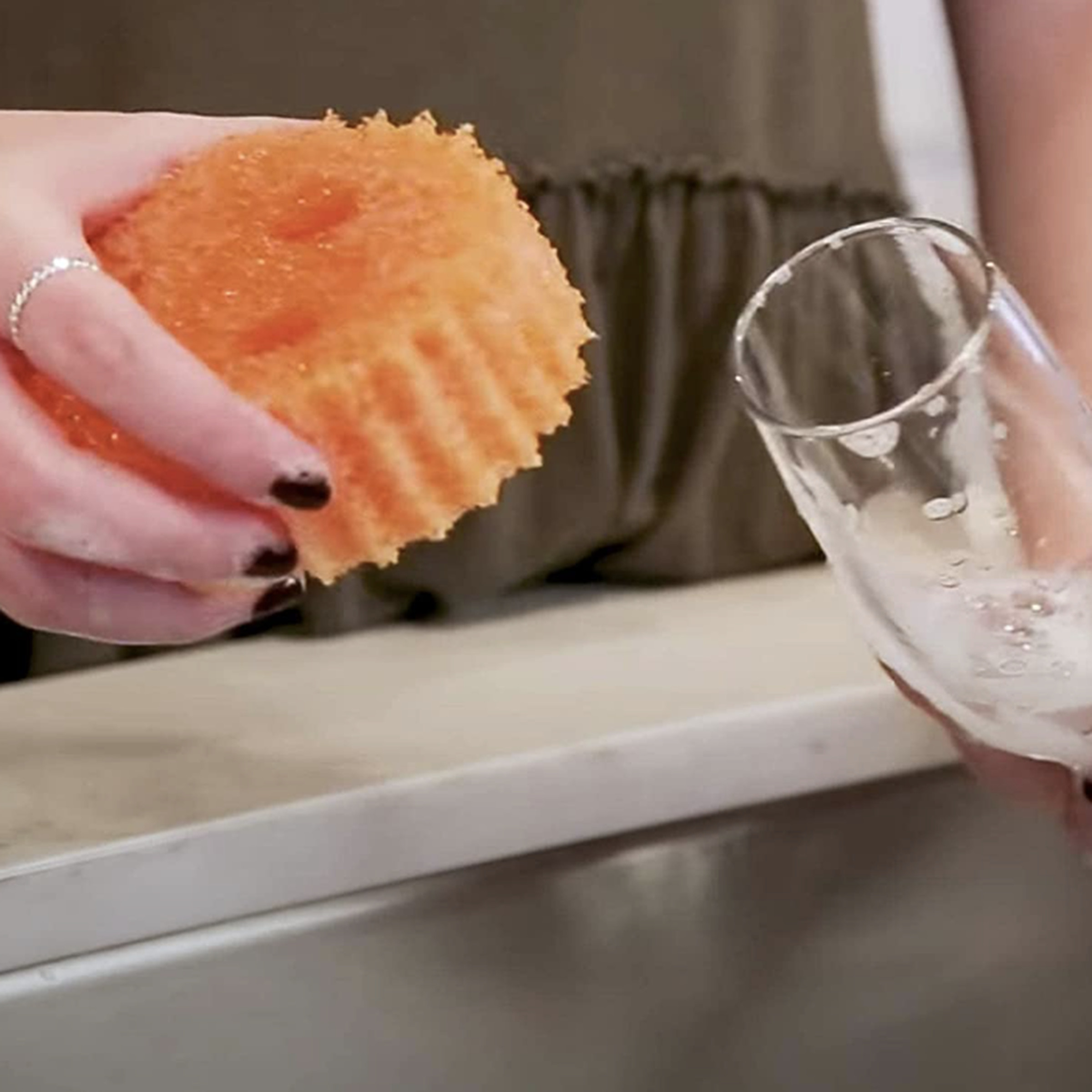 Hand holding round orange sponge and cleaning wine glass over sink.