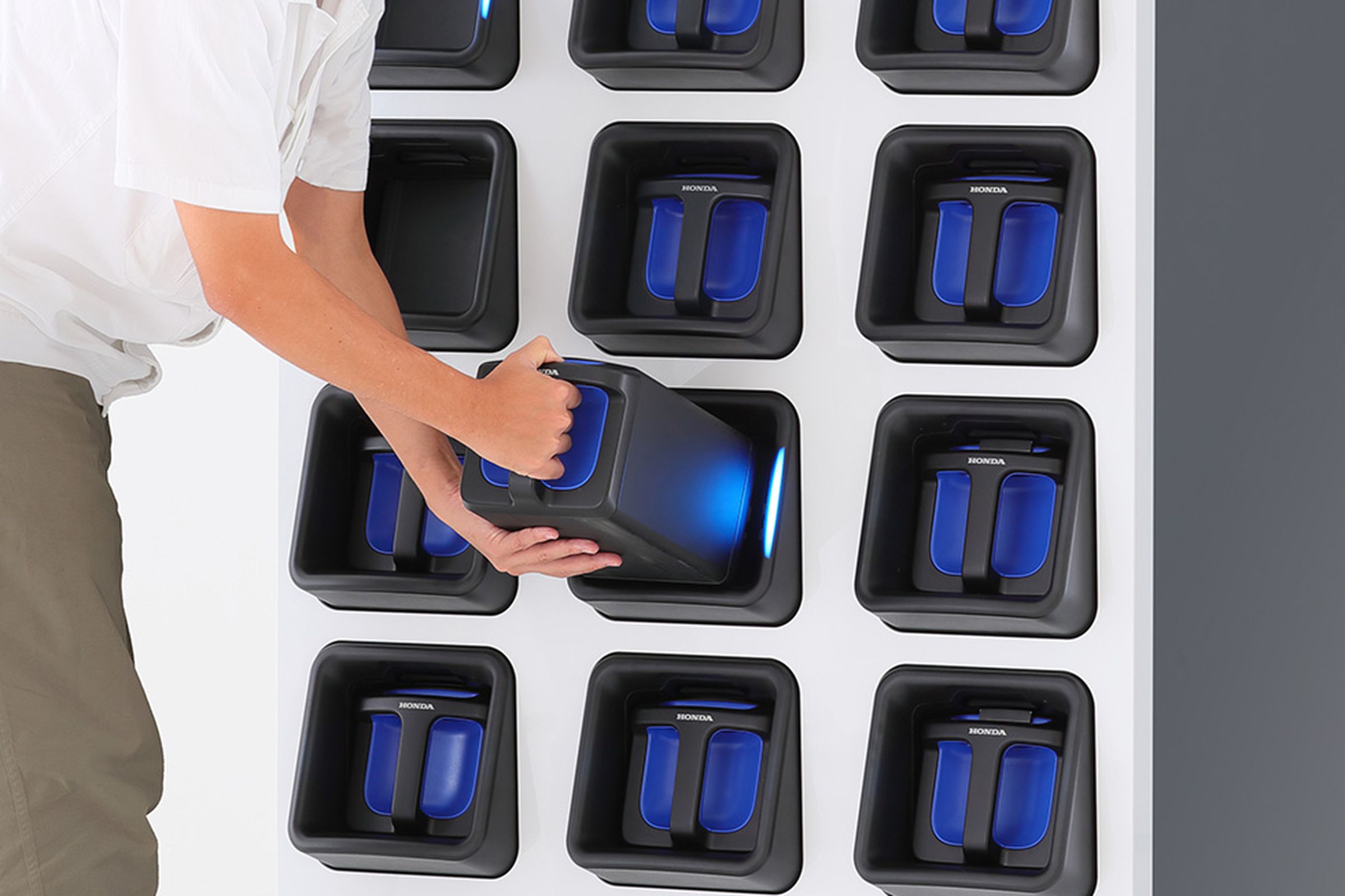 A man is pulling out a battery pack from an angled slot amongst a grid of slots that have the blue packs nestled in them.