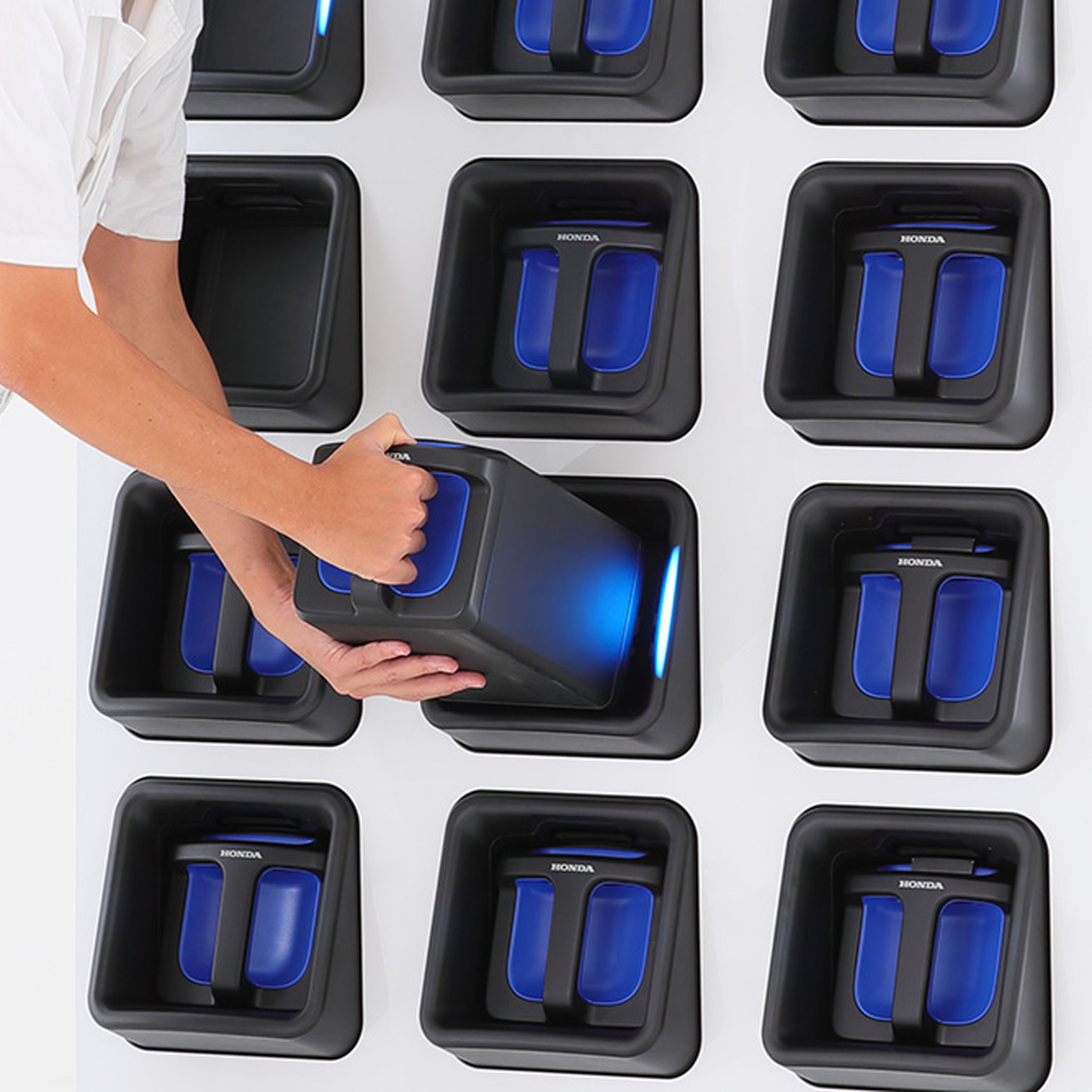 A man is pulling out a battery pack from an angled slot amongst a grid of slots that have the blue packs nestled in them.