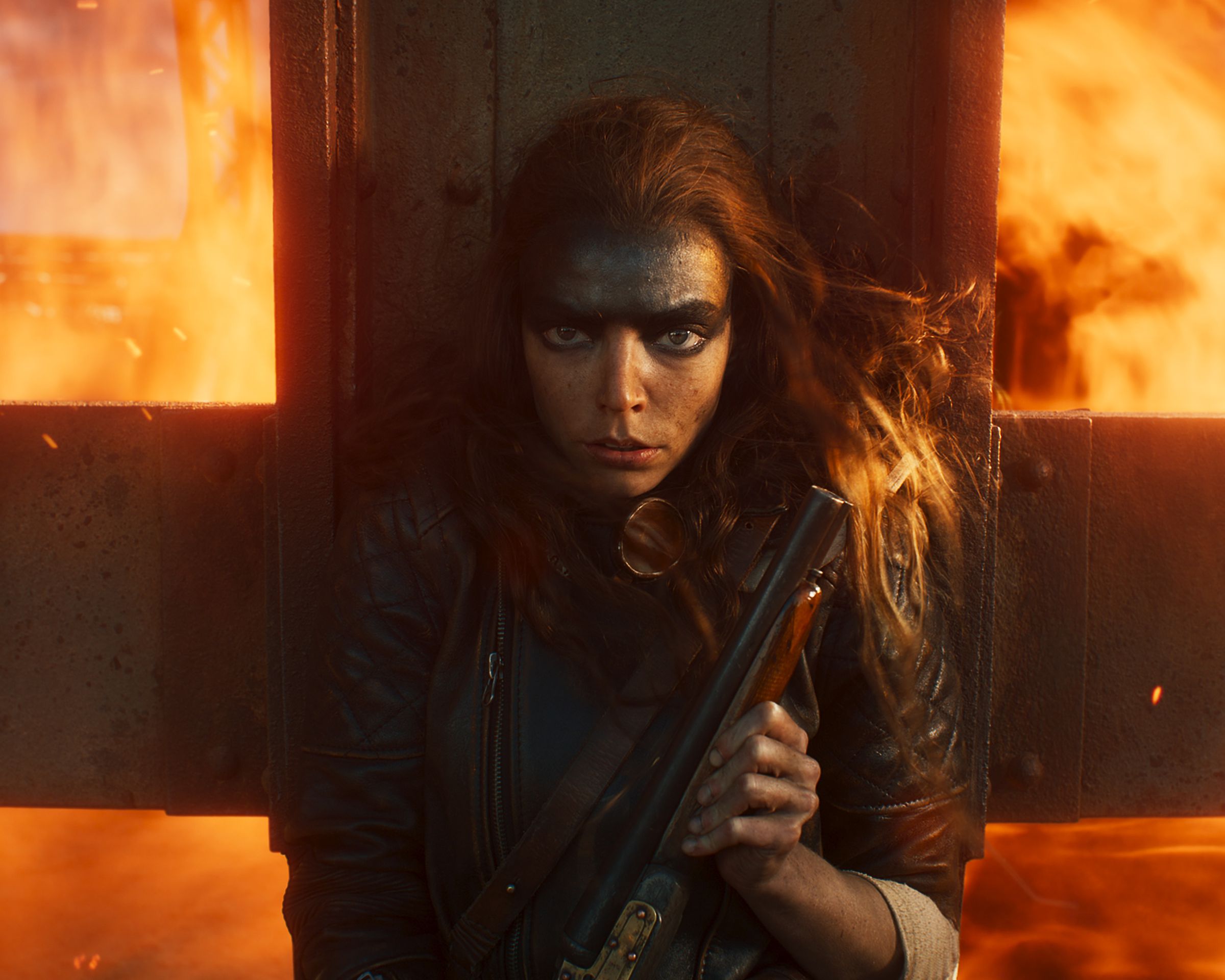 A woman clutching a shotgun to her chest while pressing up against a metal grate to protect herself from a wall of flames rushing up from behind her.