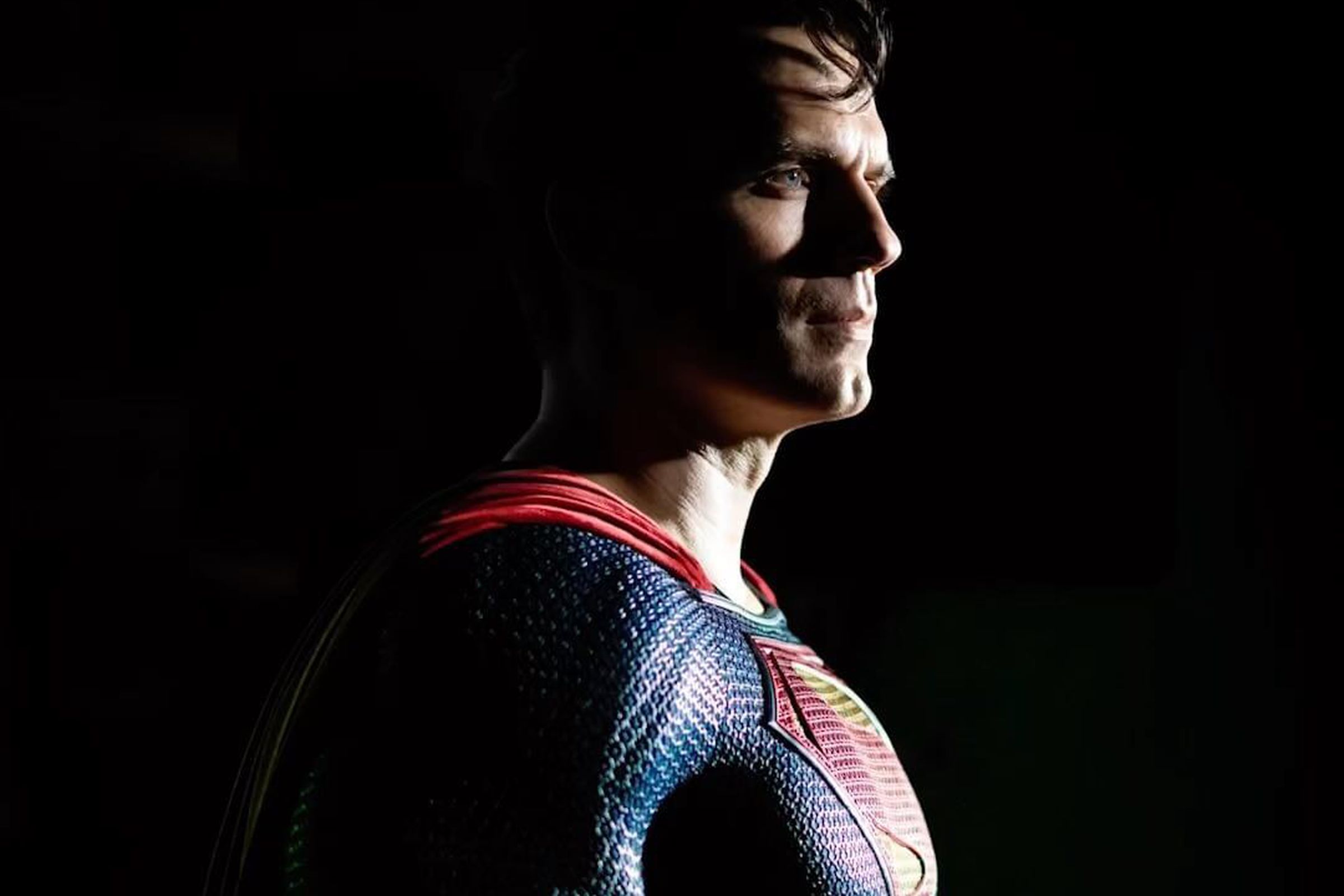 Photo of Henry Cavill dressed up as Superman, standing against a black background.