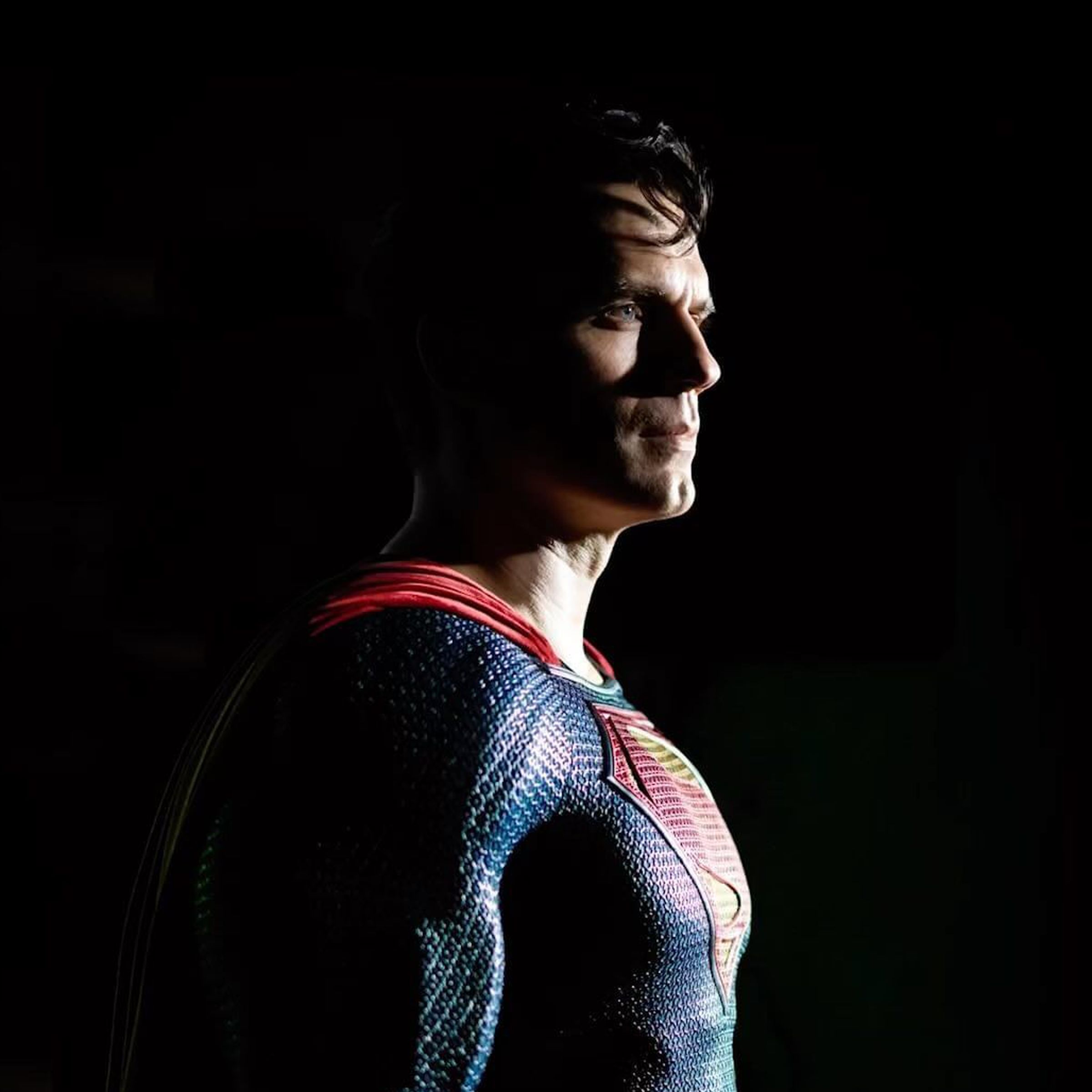 Photo of Henry Cavill dressed up as Superman, standing against a black background.