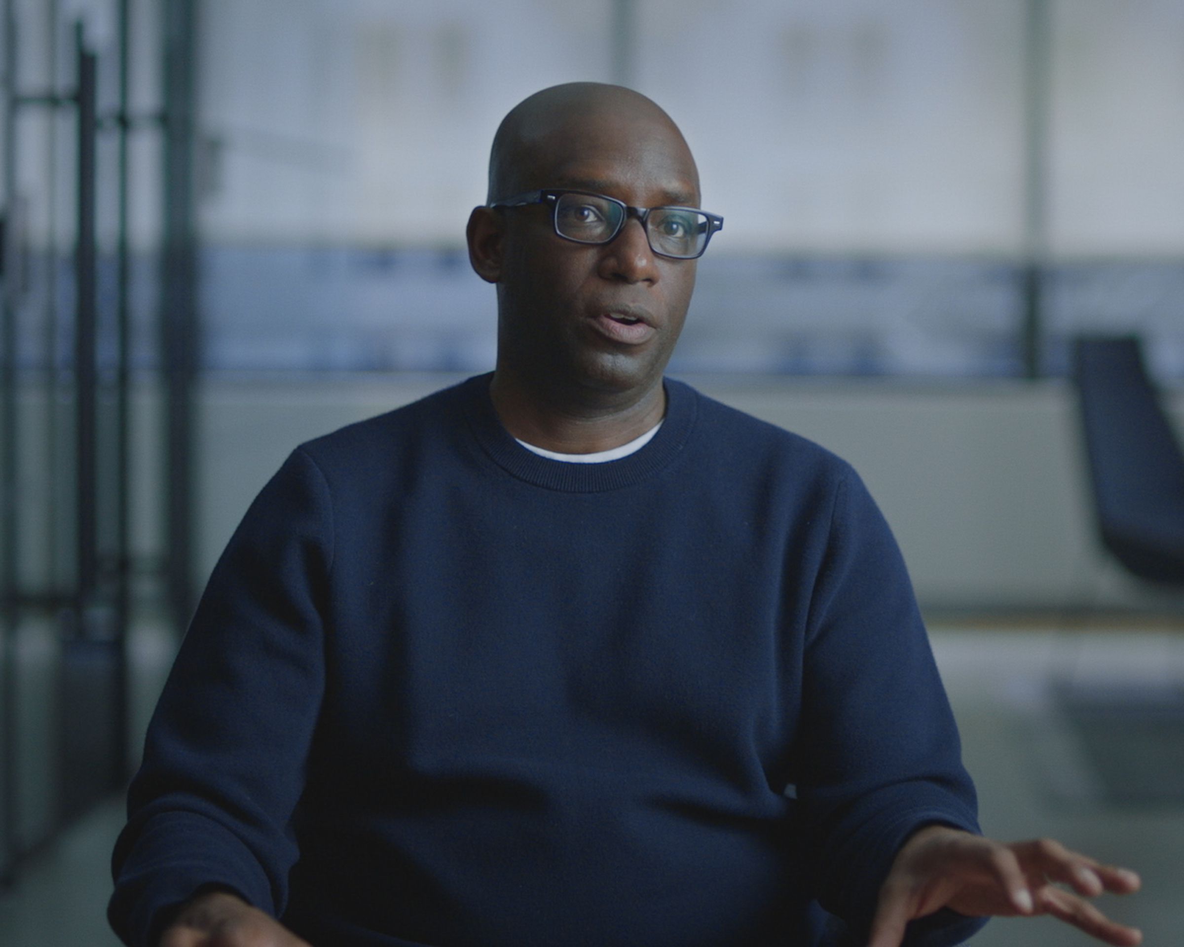 A bald man wearing glasses and a blue sweater in a boardroom.